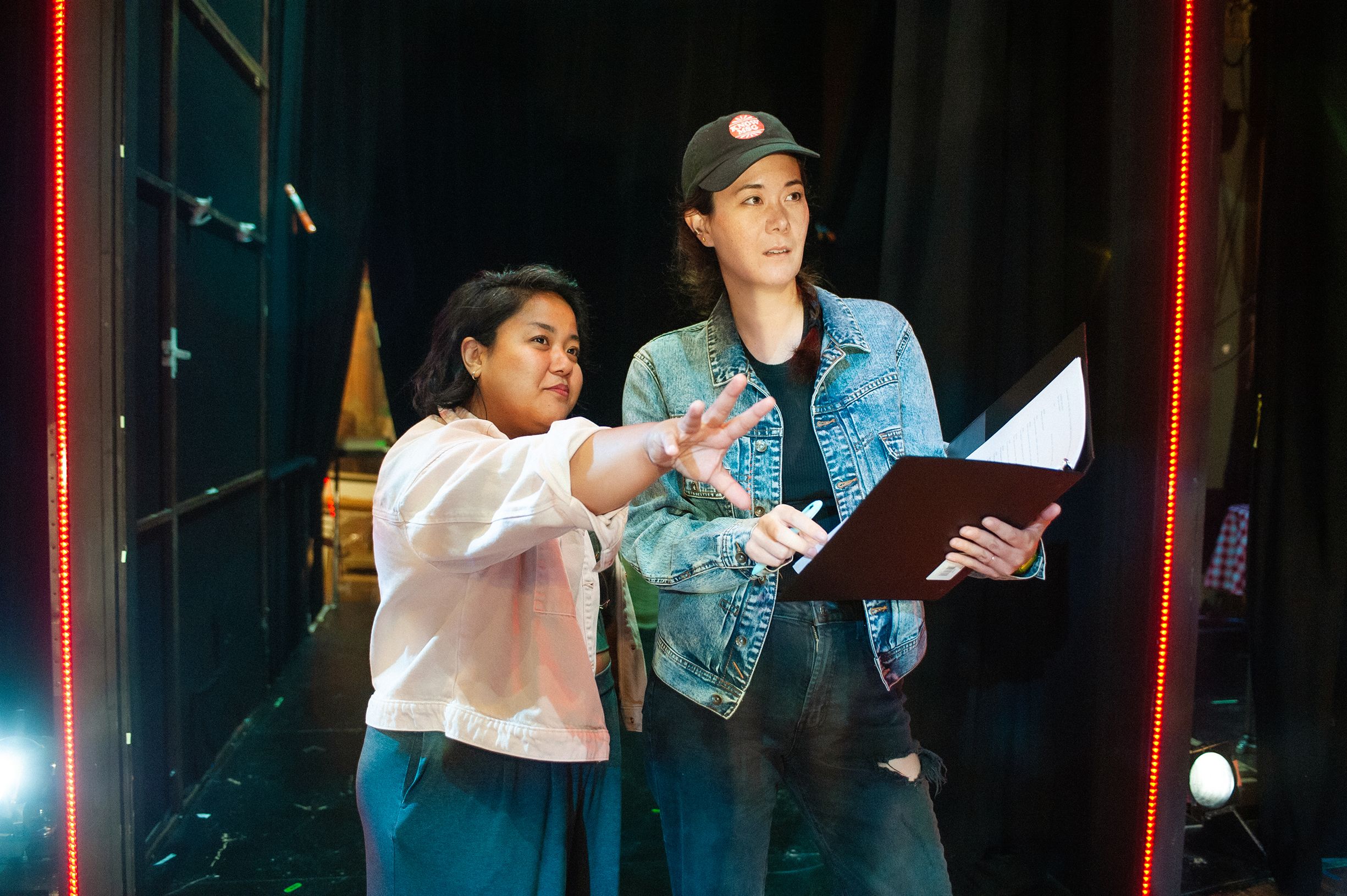 Photo of two women looking at the stage while holding a binder open