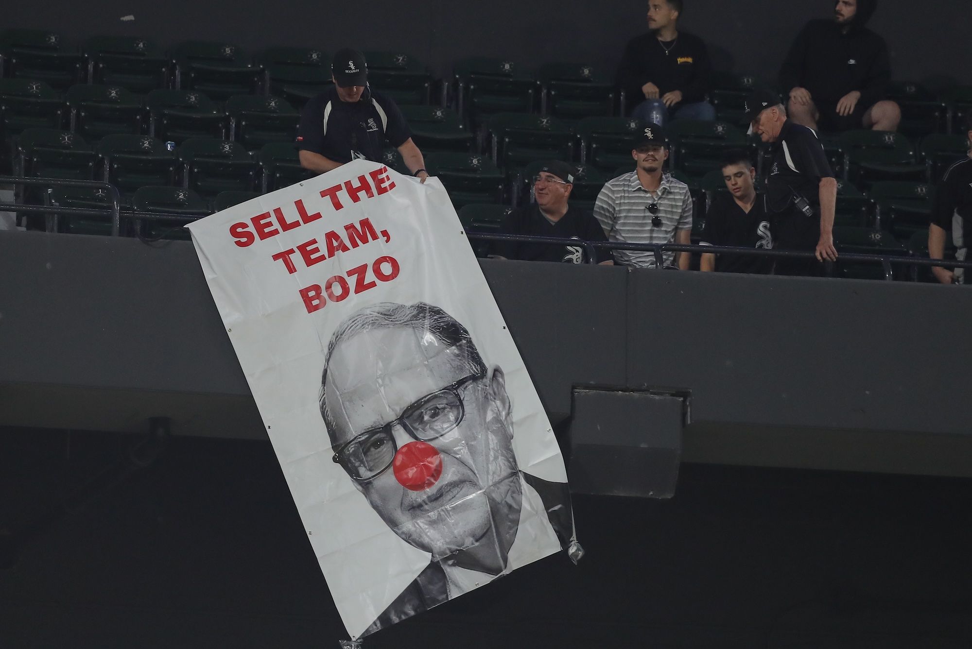 A White Sox fan holding a sign that reads Sell The Team, Bozo with a picture of Jerry Reinsdorf with a clown nose.