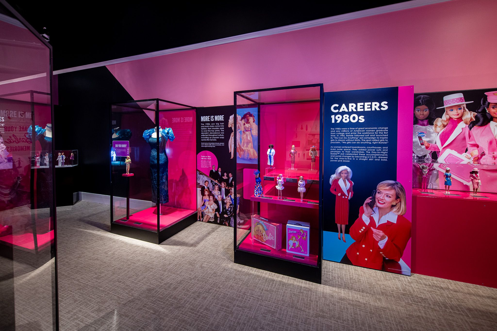 Gallery with pink and magenta walls, glass cases displaying Barbie dolls; a bold blue panel reads "CAREERS 1980s" beside images of dolls and mannequins.
