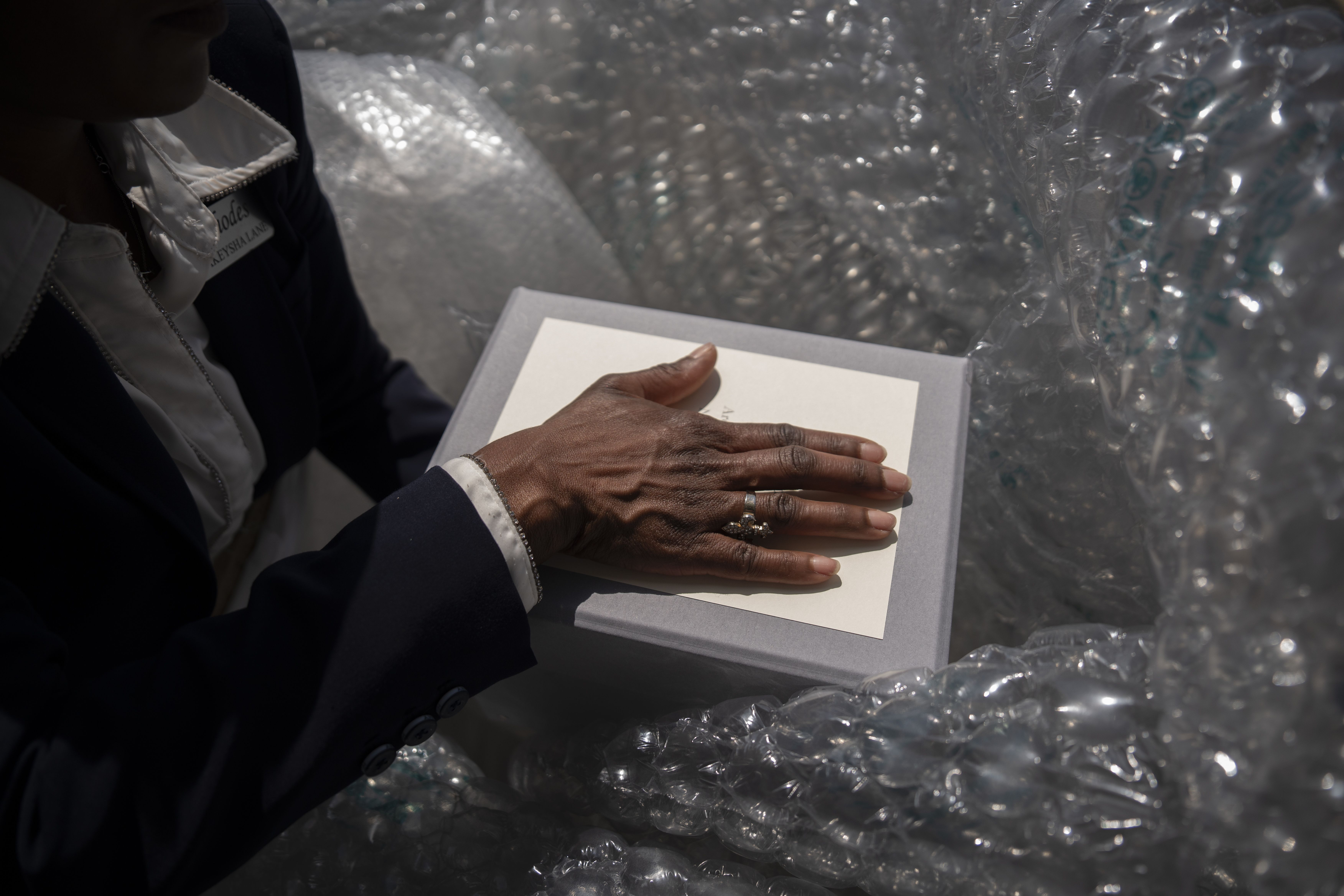 A hand rests on the top of a box as it is removed from bubble wrap.