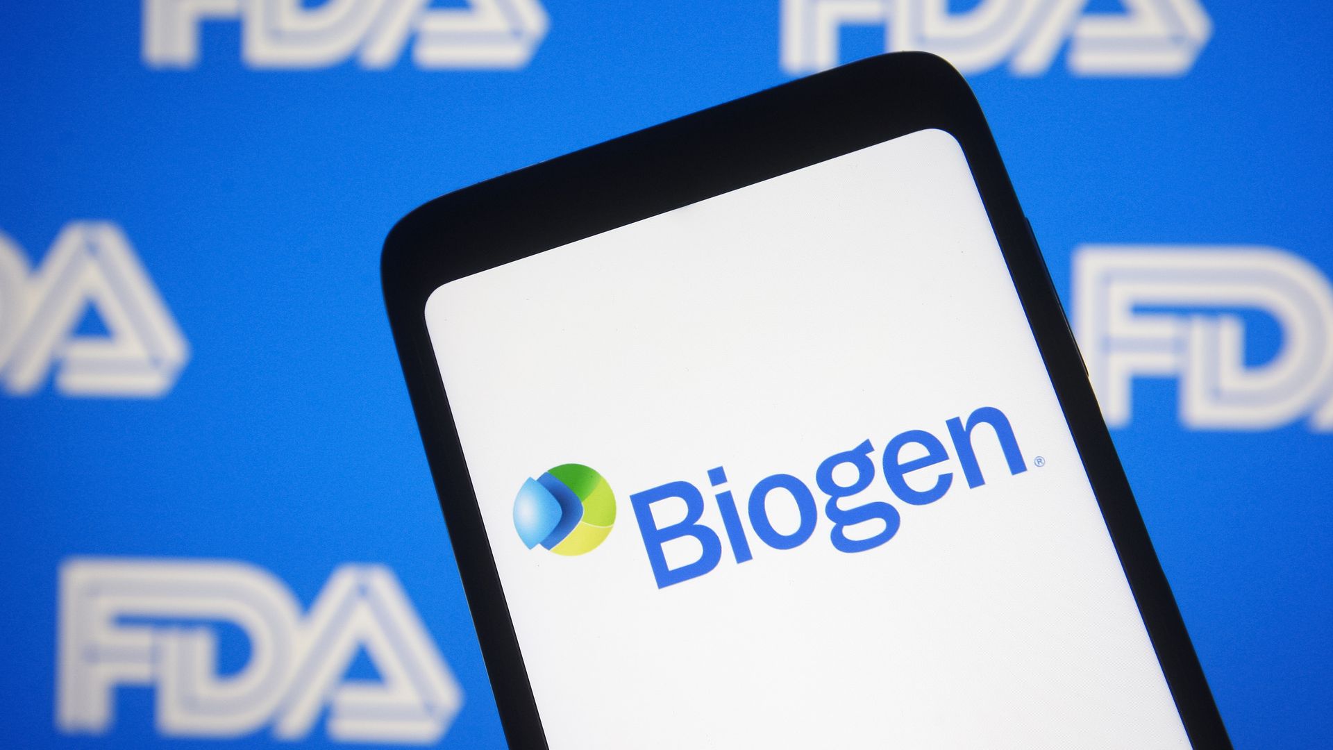 An image of the Biogen logo on a smart phone in front of the FDA logo in the background.