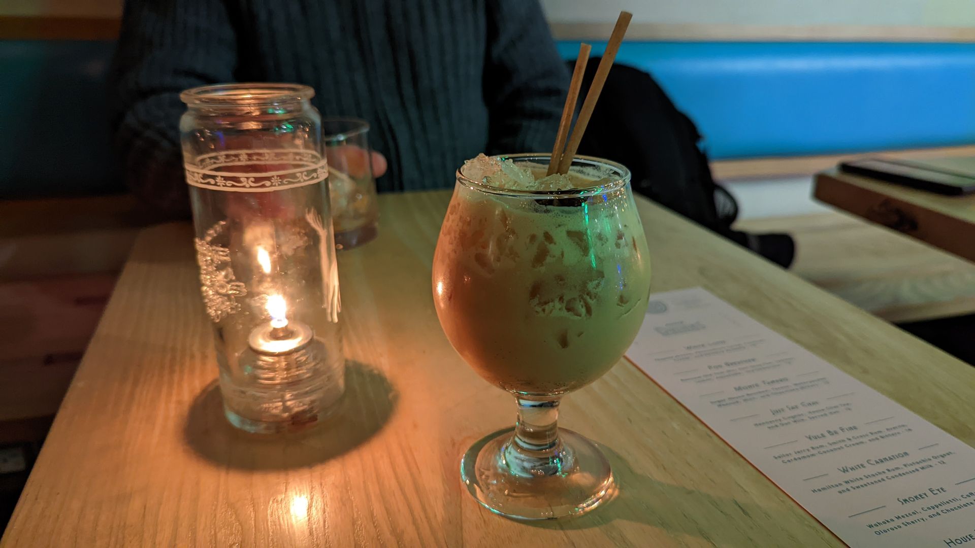 A cocktail sits on a table next to an oil lamp.