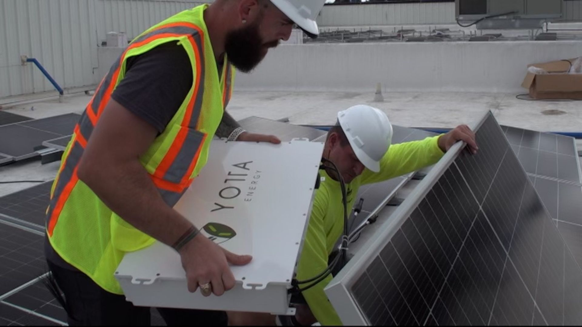 Workers installing a Yotta Energy battery system behind solar panels.