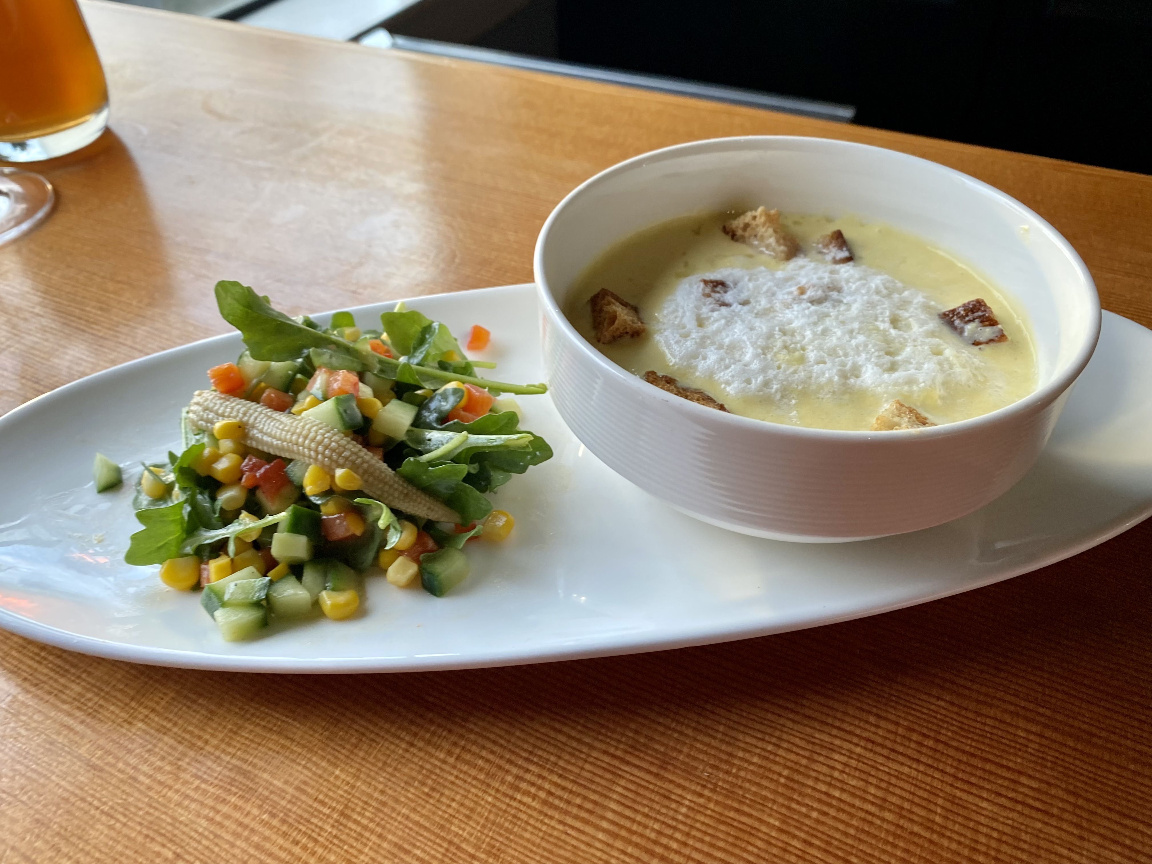A salad of summer vegetables on an oblong plate next to a bowl filled with yellow corn soup.