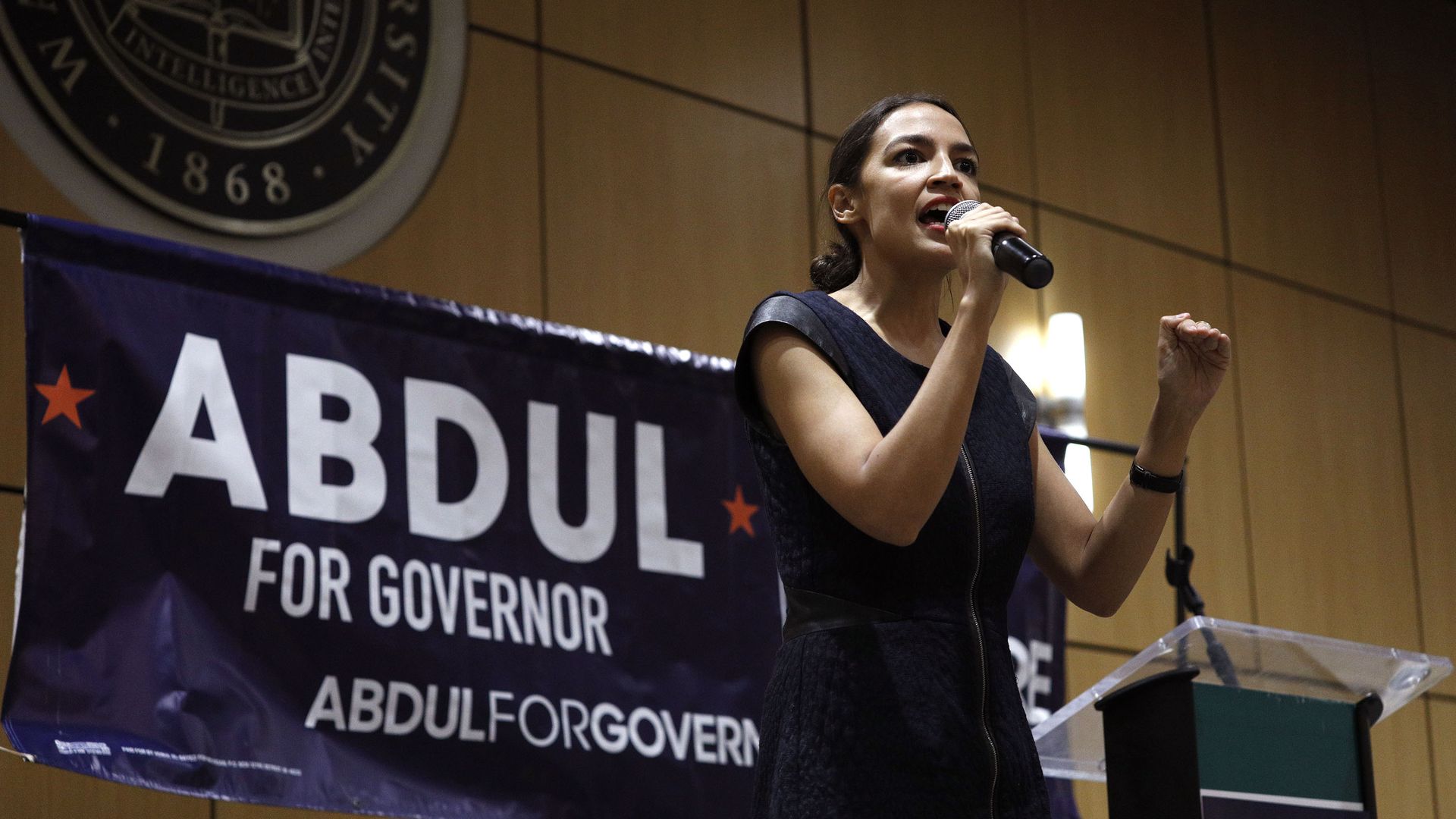 Alexandria Ocasio-Cortez on stage in front of an Abdul for Governor poster