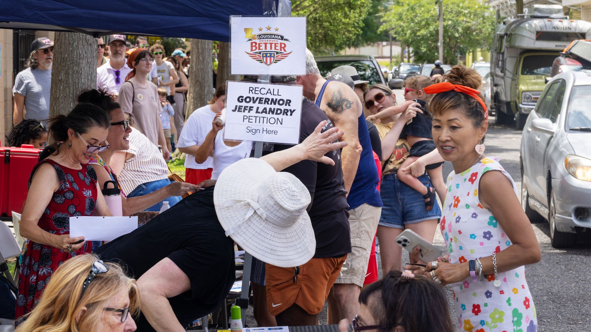 Image shows people outside around a tent. There are signs that say "Louisiana Deserves Better" and "Recall Governor Jeff Landry petition."