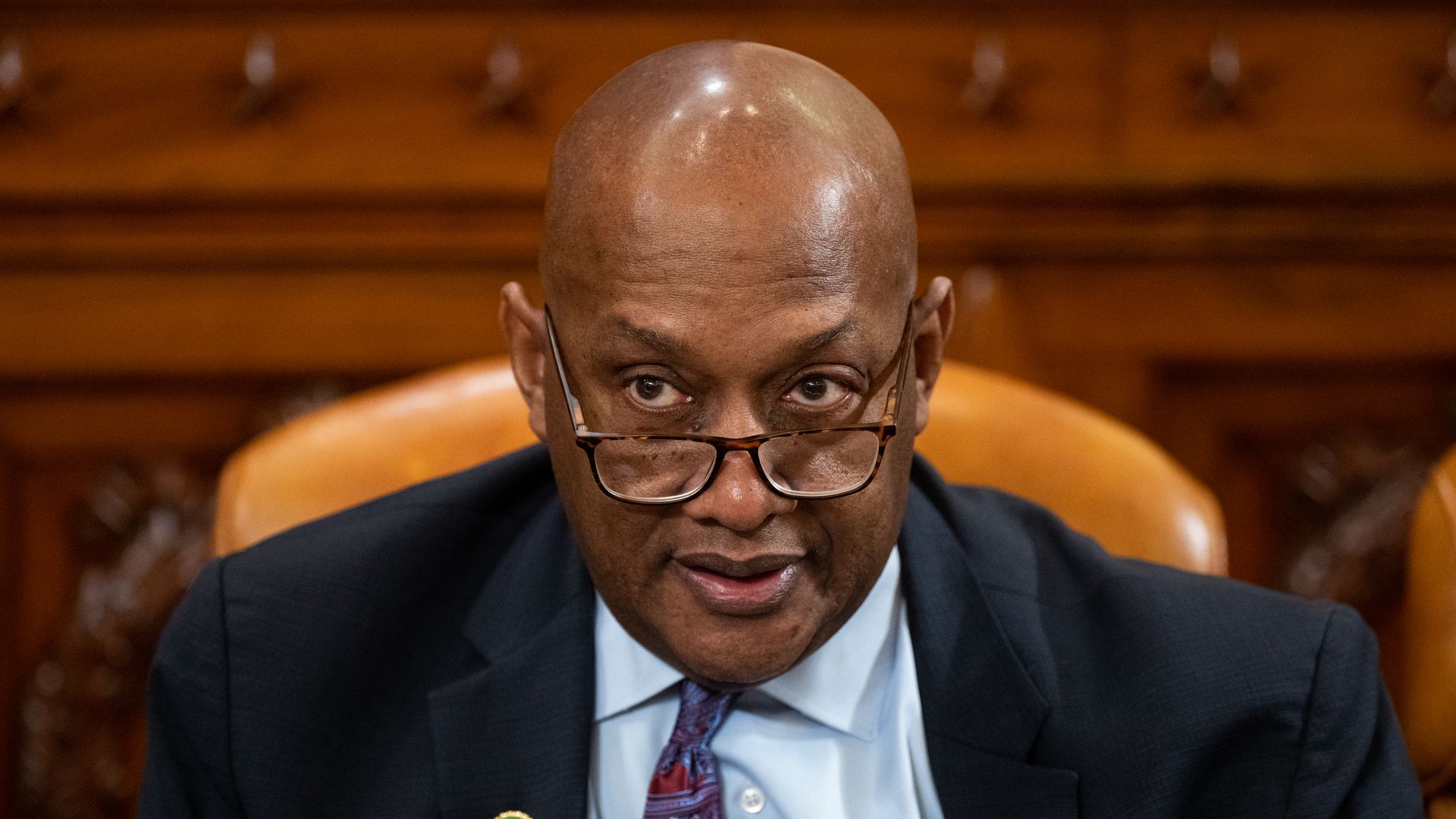Rep. Dwight Evans wearing a dark gray suit and sitting in an orange leather chair in front of a wooden dais.