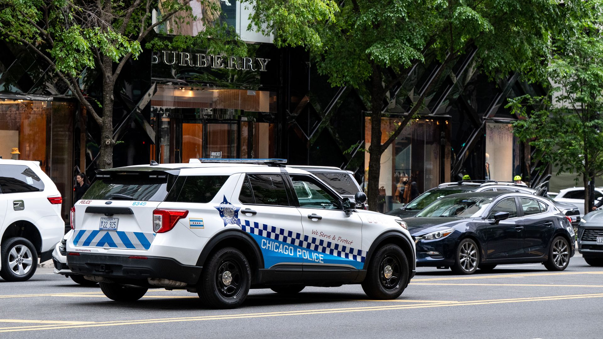 Photo of a police cruiser parked in the middle of a street as cars pass by.