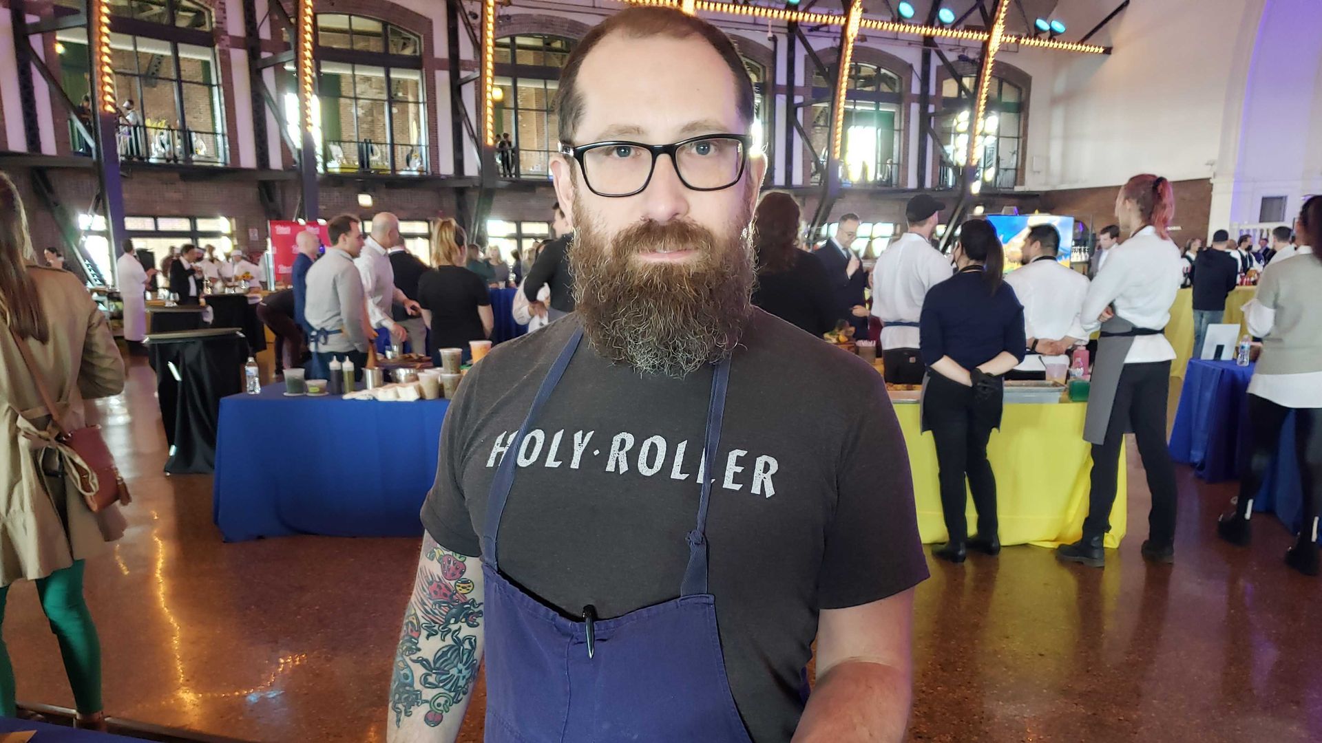 Photo of a man in an apron holding an appetizer. 