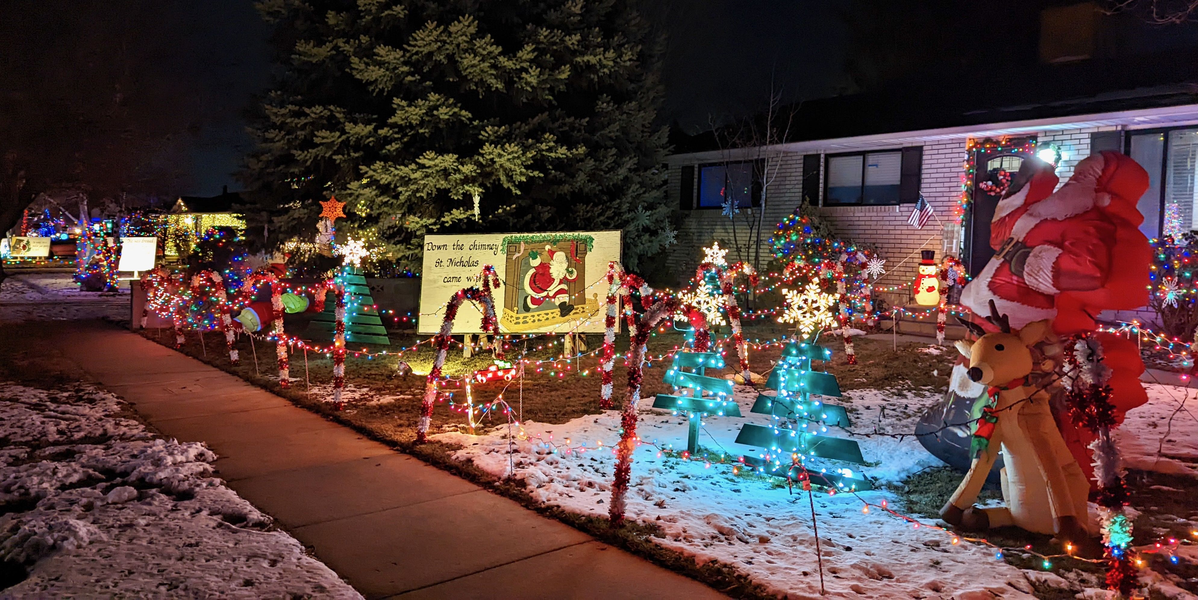 A residential yard lighted with Christmas decorations and a placard showing a verse from "The Night Before Christmas."