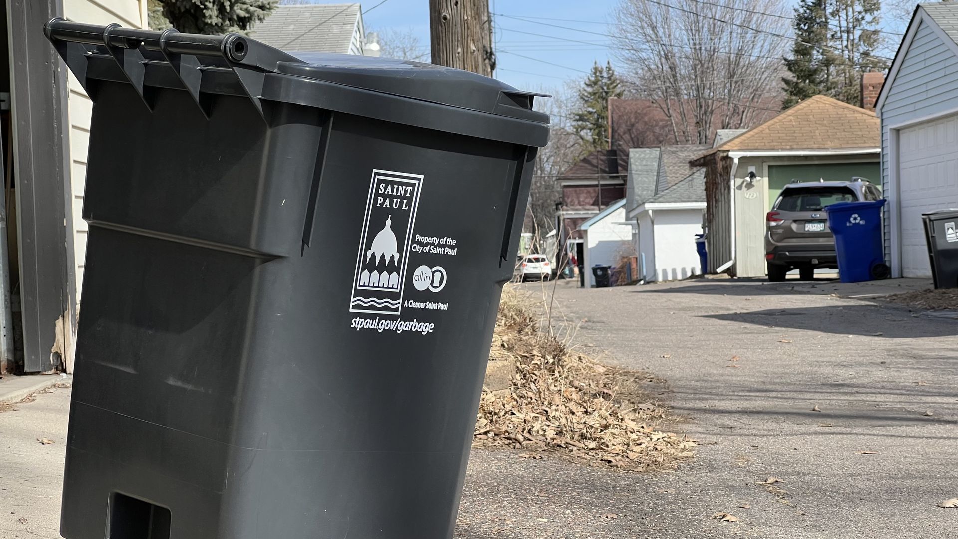 A black trash bin that says "Saint Paul" on the side sits in an alley