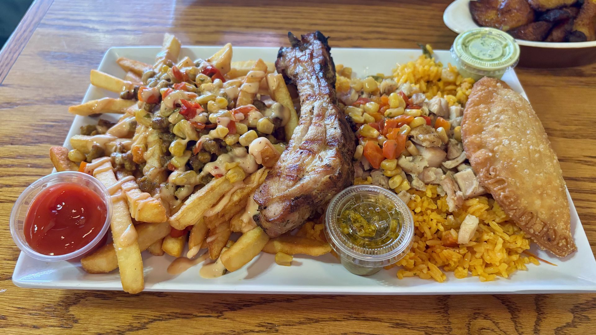 A sampler platter at Barroluco, with loaded fries, a pork rib, paella and a chicken-and-cheese empanada, along with three different sauce containers.