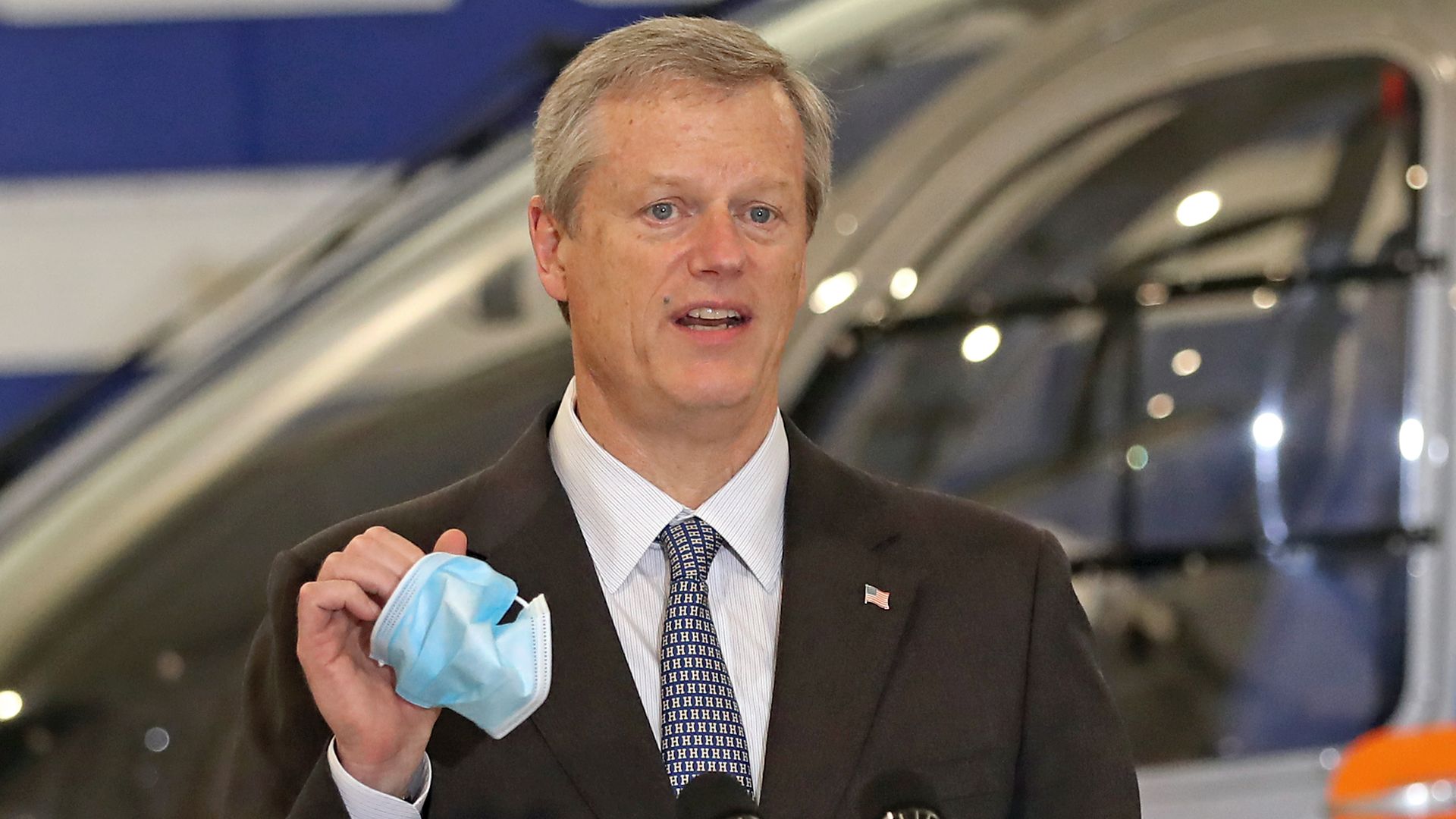 Charlie Baker in a suit and tie, holding a face mask 