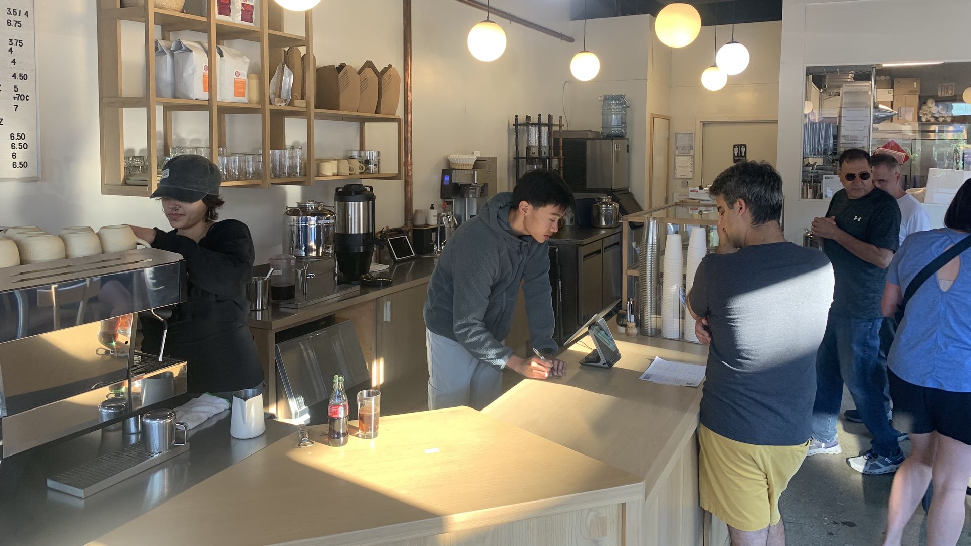 Photo of people waiting in a line near a counter where baristas make coffee. 