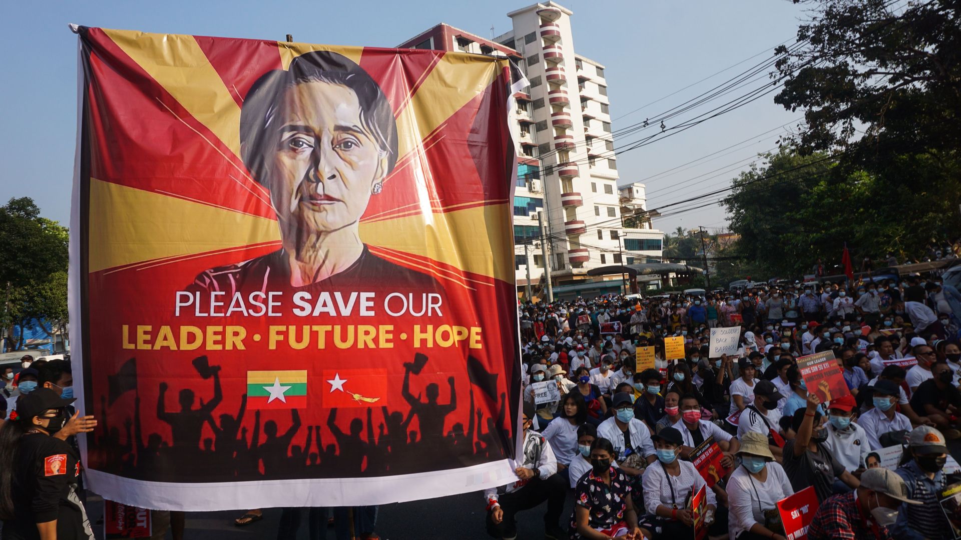 Picture of protesters in Myanmar holding a sign of Aung San Suu Kyi that says "Please save our leader"