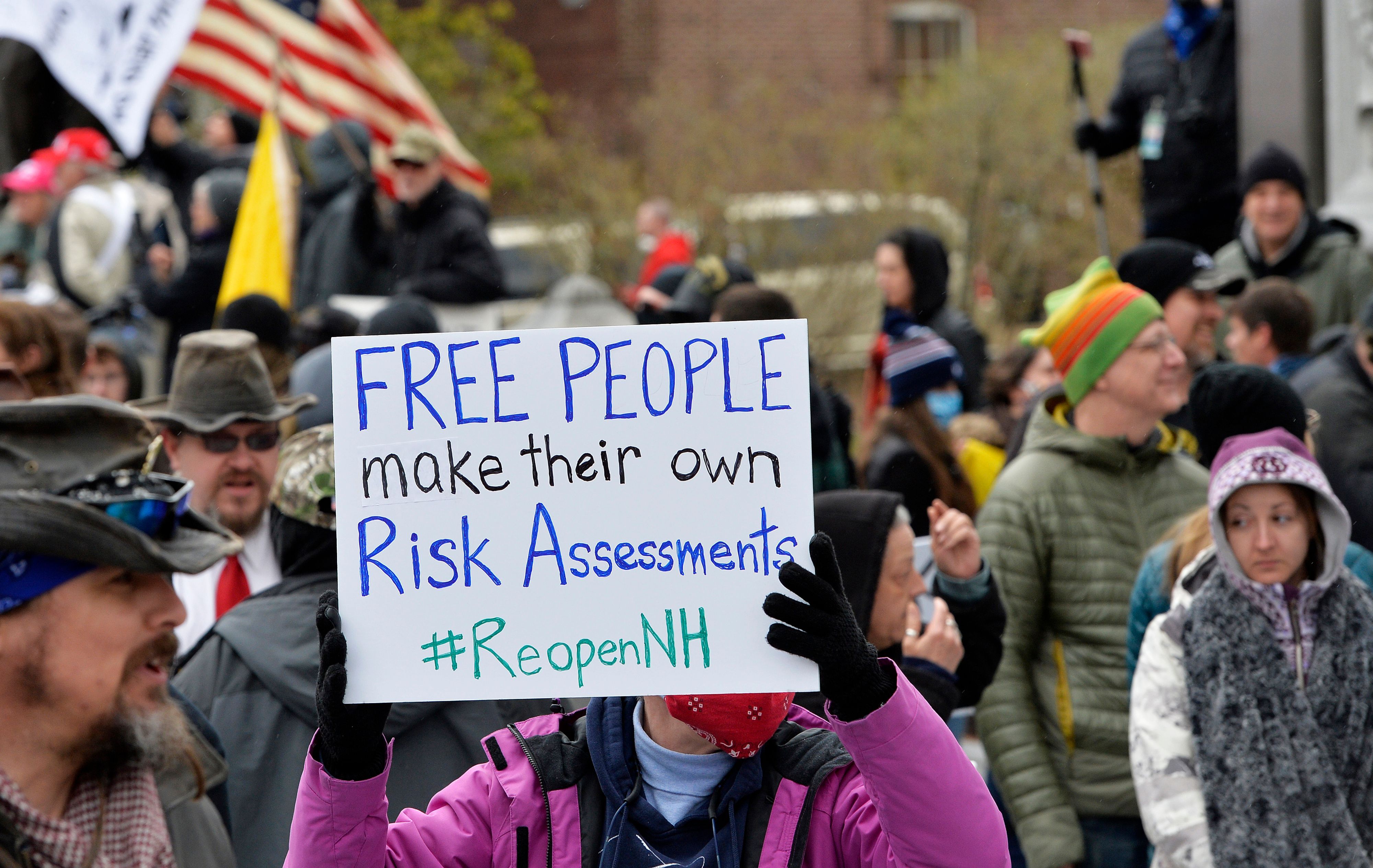 In this image, a person holds a sign that reads "free people make their own risk assessments" 