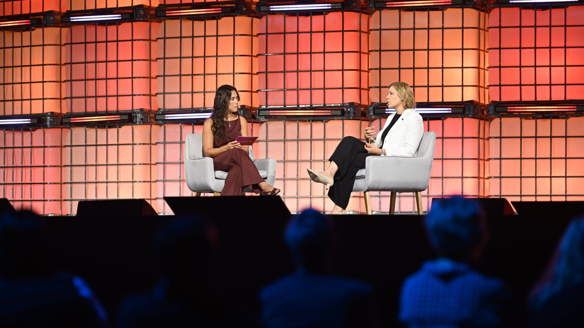 Two people sitting in chairs talk on a stage