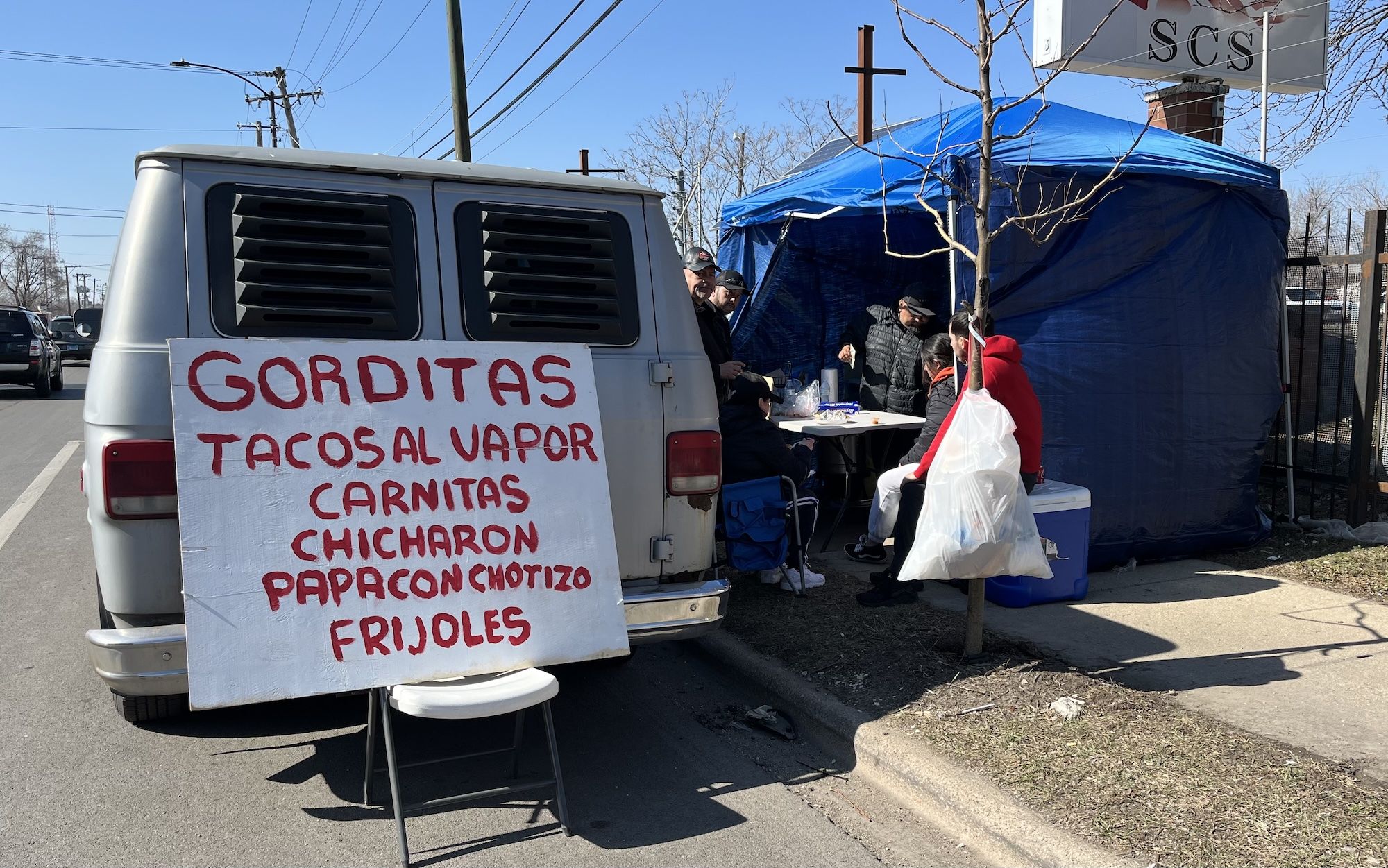 Van with sign in the back listing different foods for sale.