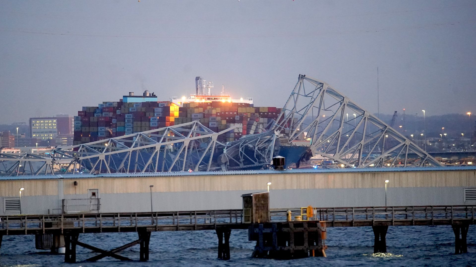 A container ship is shown below the crumbled Francis Scott Key bridge in Baltimore, Maryland, after dawn.