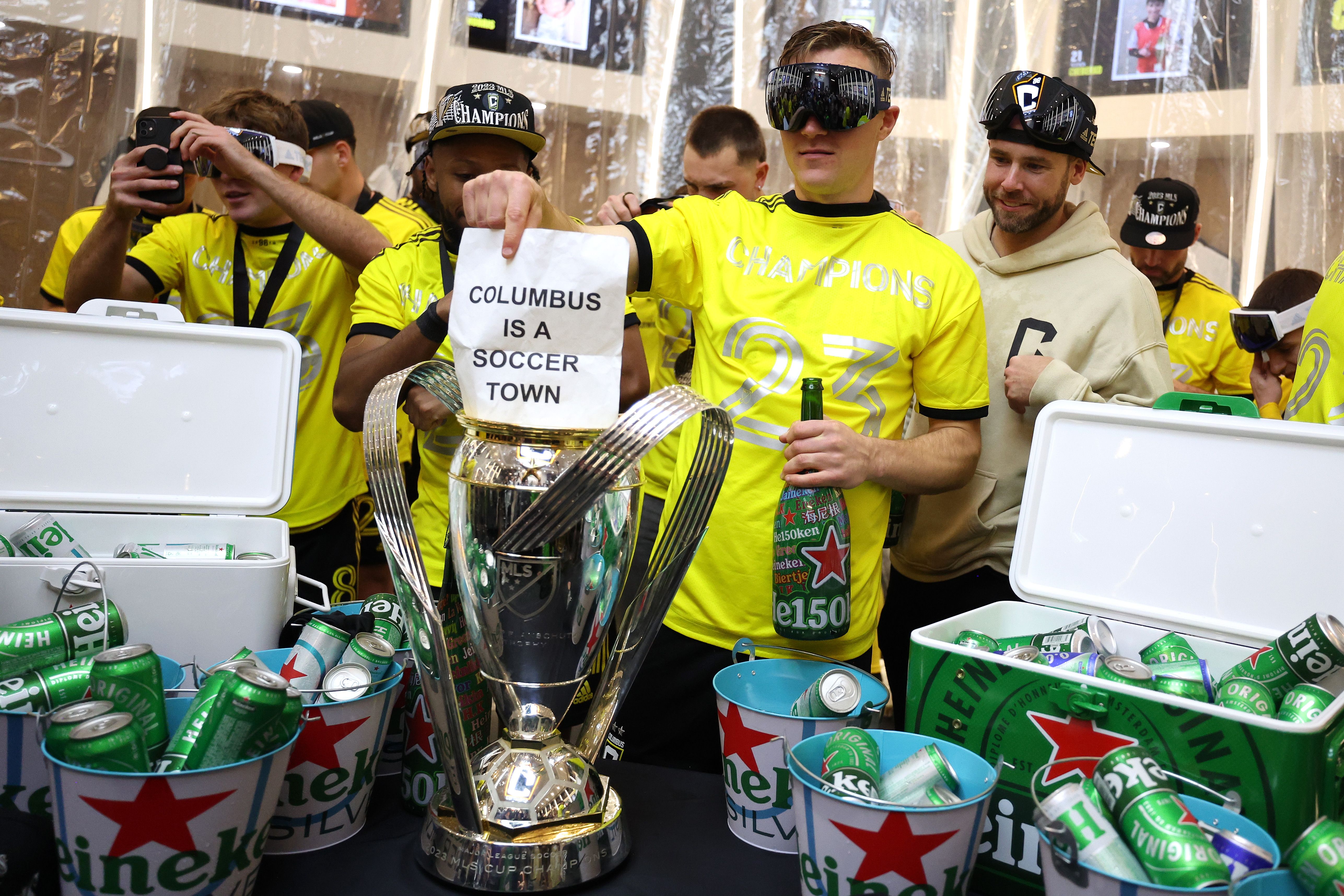 A Crew player holds a sign reading "Columbus is a soccer town" in front of the Philip F. Anschutz Trophy