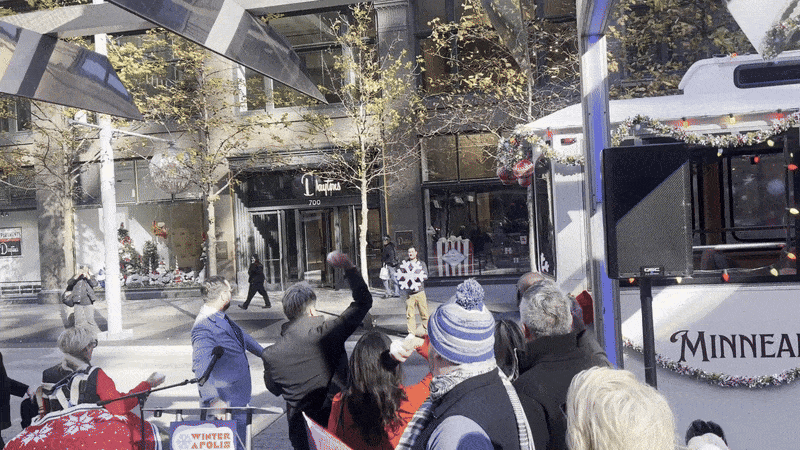 People throwing snowballs at a man holding a large snowflake ornament, with a trolly to the side. 
