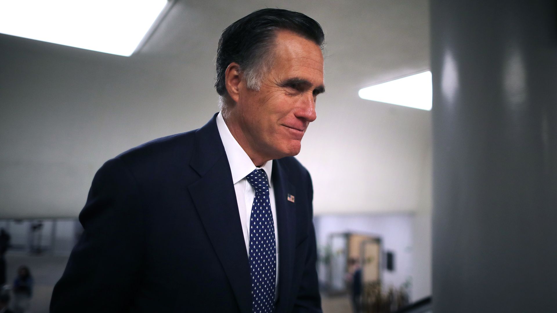 In this image, Romney walks through a hallway wearing a suit 