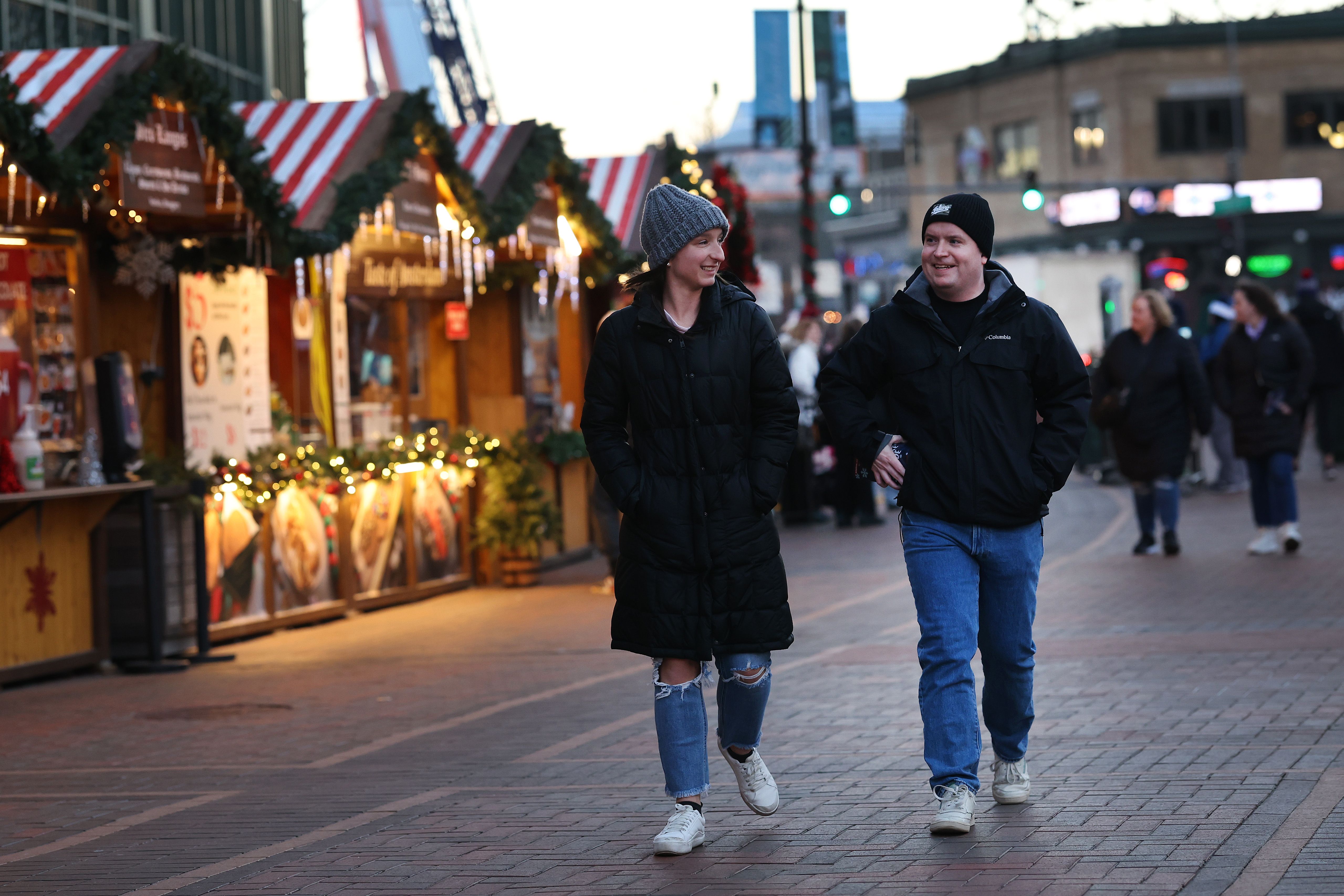 Photo of two people walking along a plaza looking at shops. 