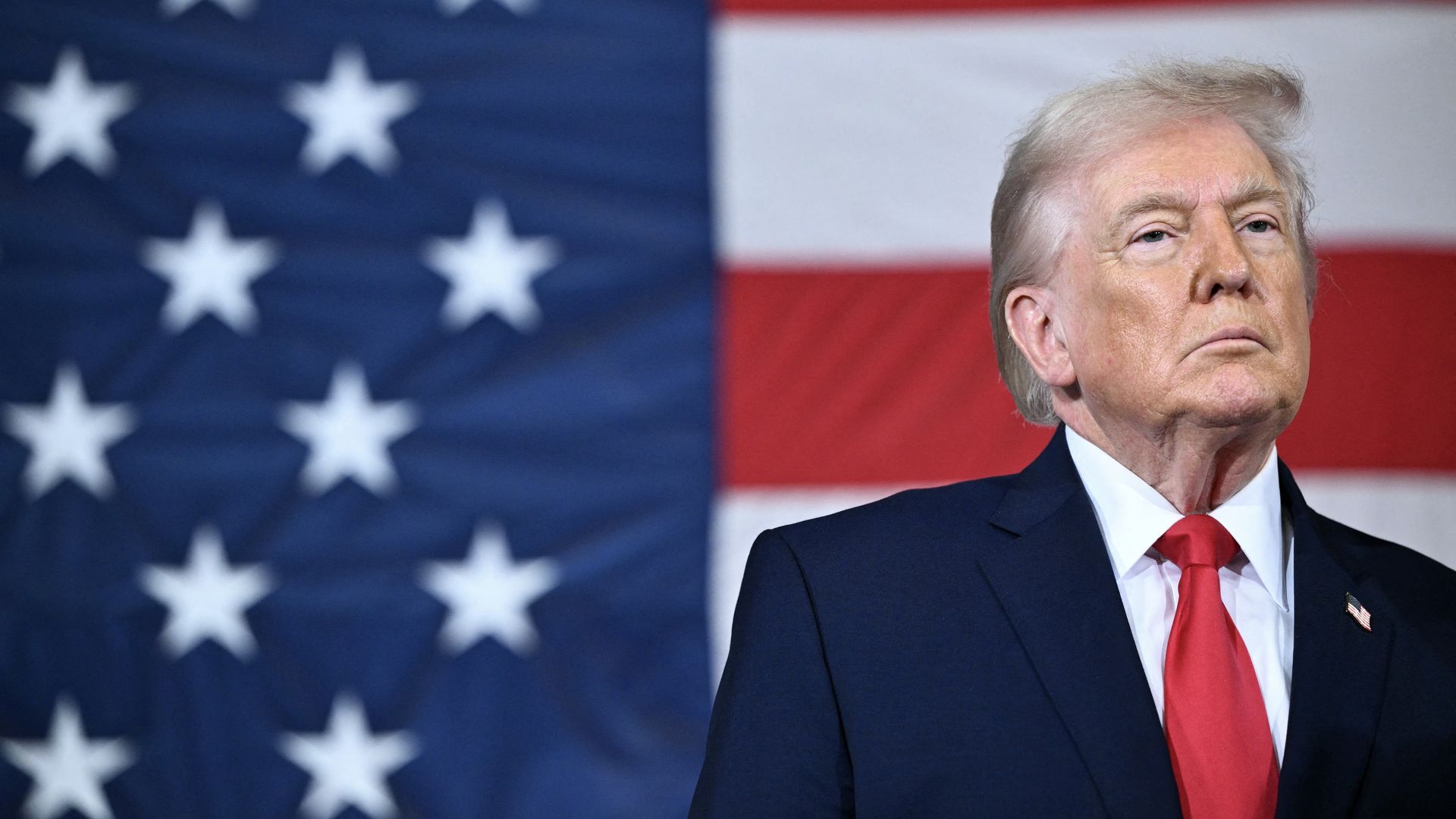 President Donald Trump standing on a stage at Fort Bragg, North Carolina, with members of the military and families in the background.