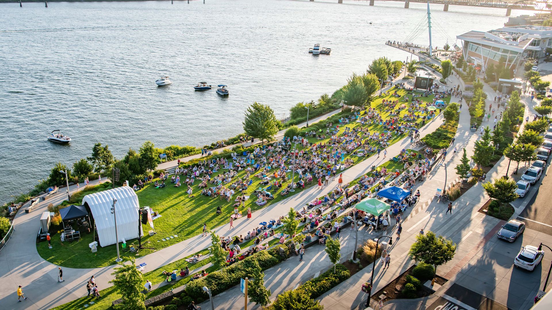 An aerial photo of a large group of people gathered in front of a stage that is along a waterfront.