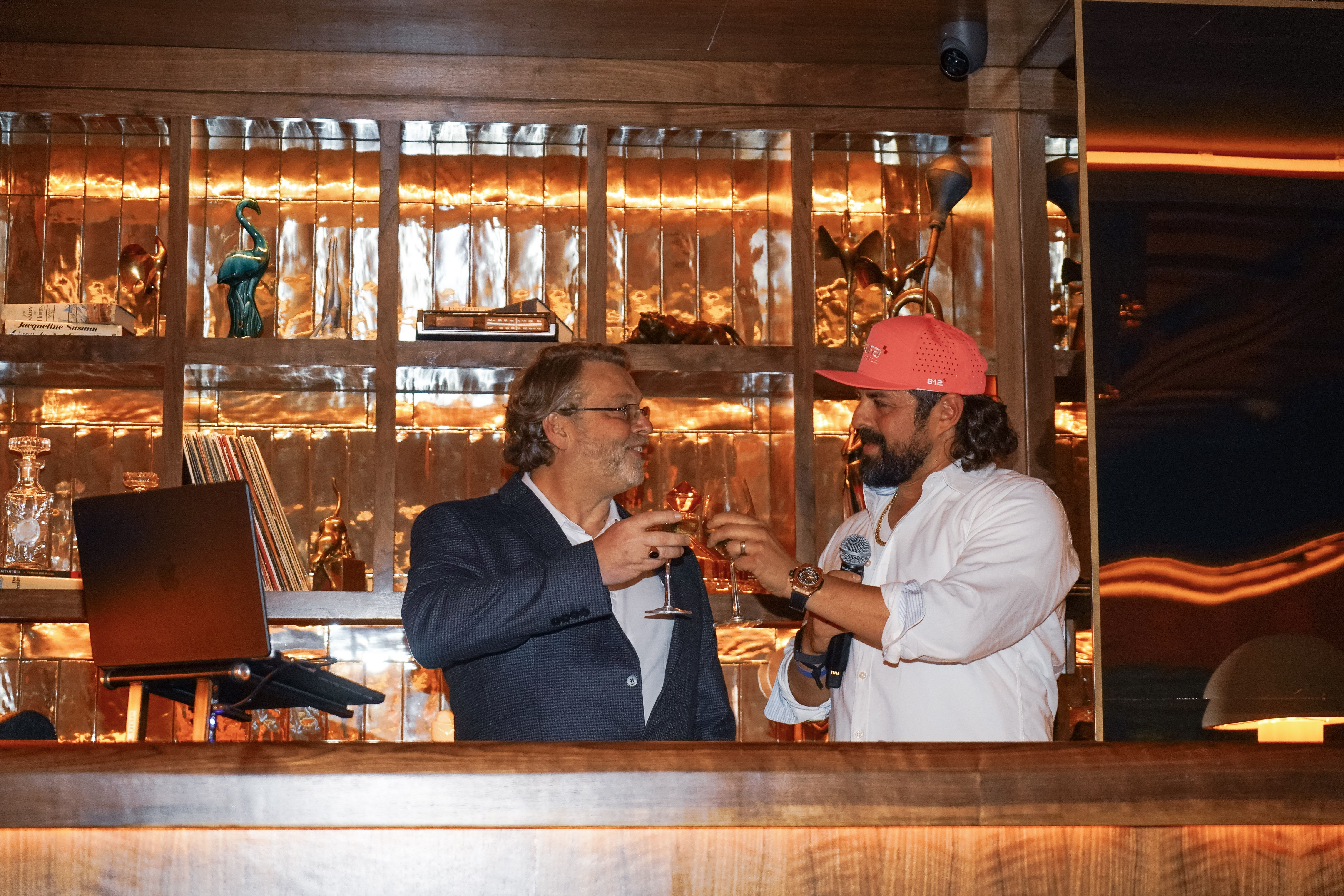 A photo of two men clinking their glasses together in a bar