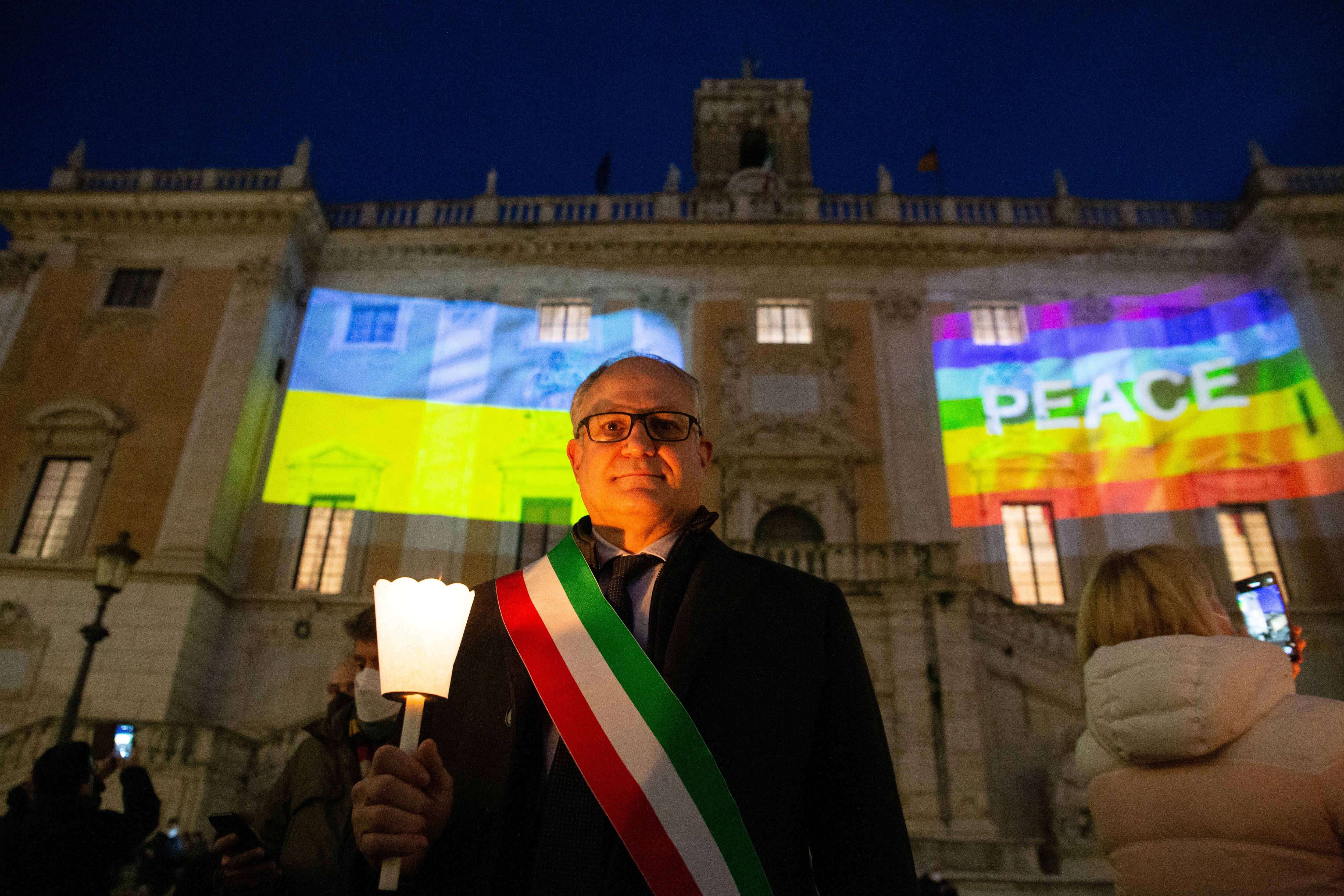 Photo of a person wearing the Italian colors in a strap as they hold a candle in front of a cathedral