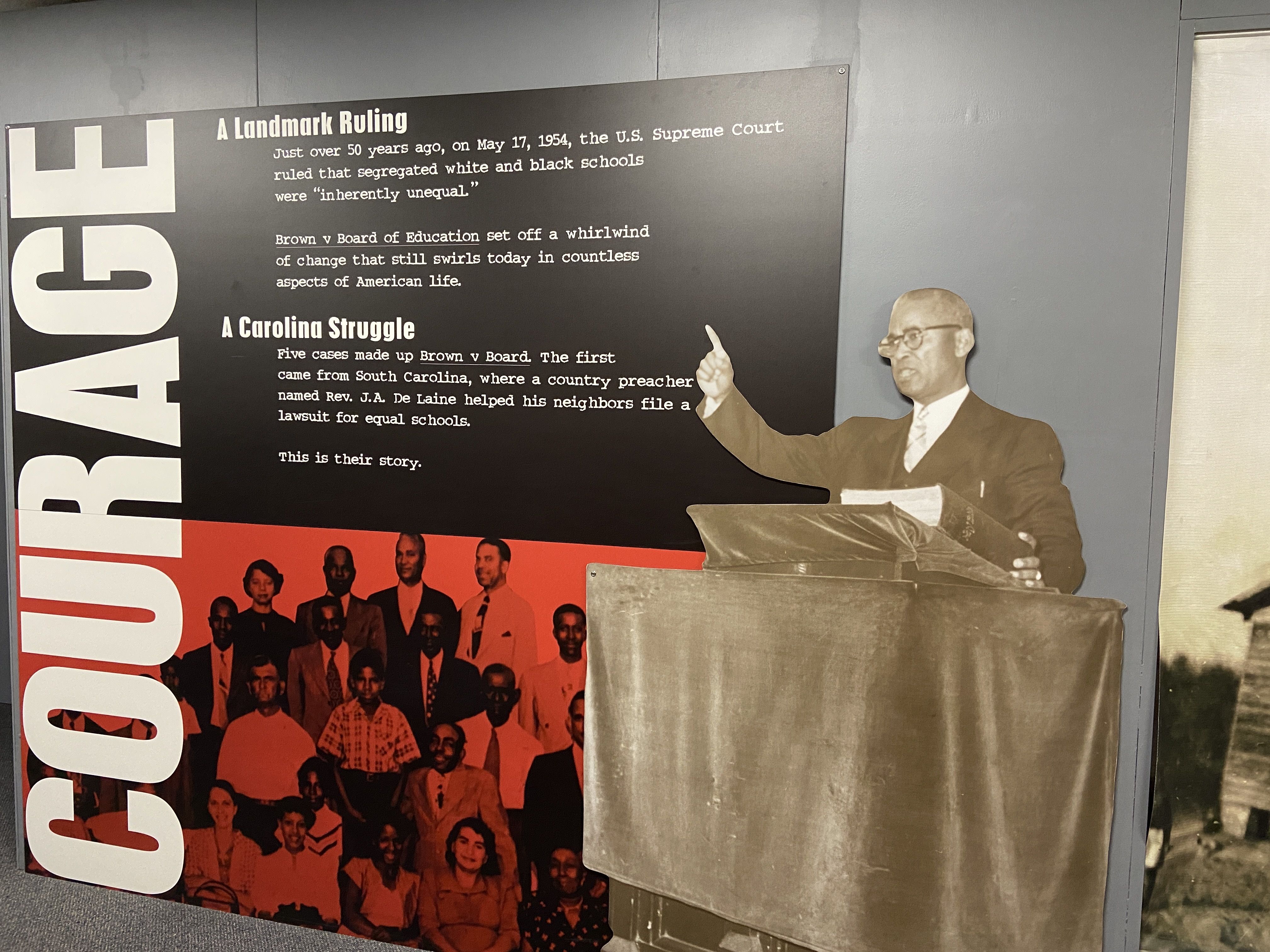 The "COURAGE" exhibit at Johnson C. Smith University shows a cutout image of Rev. De Laine.