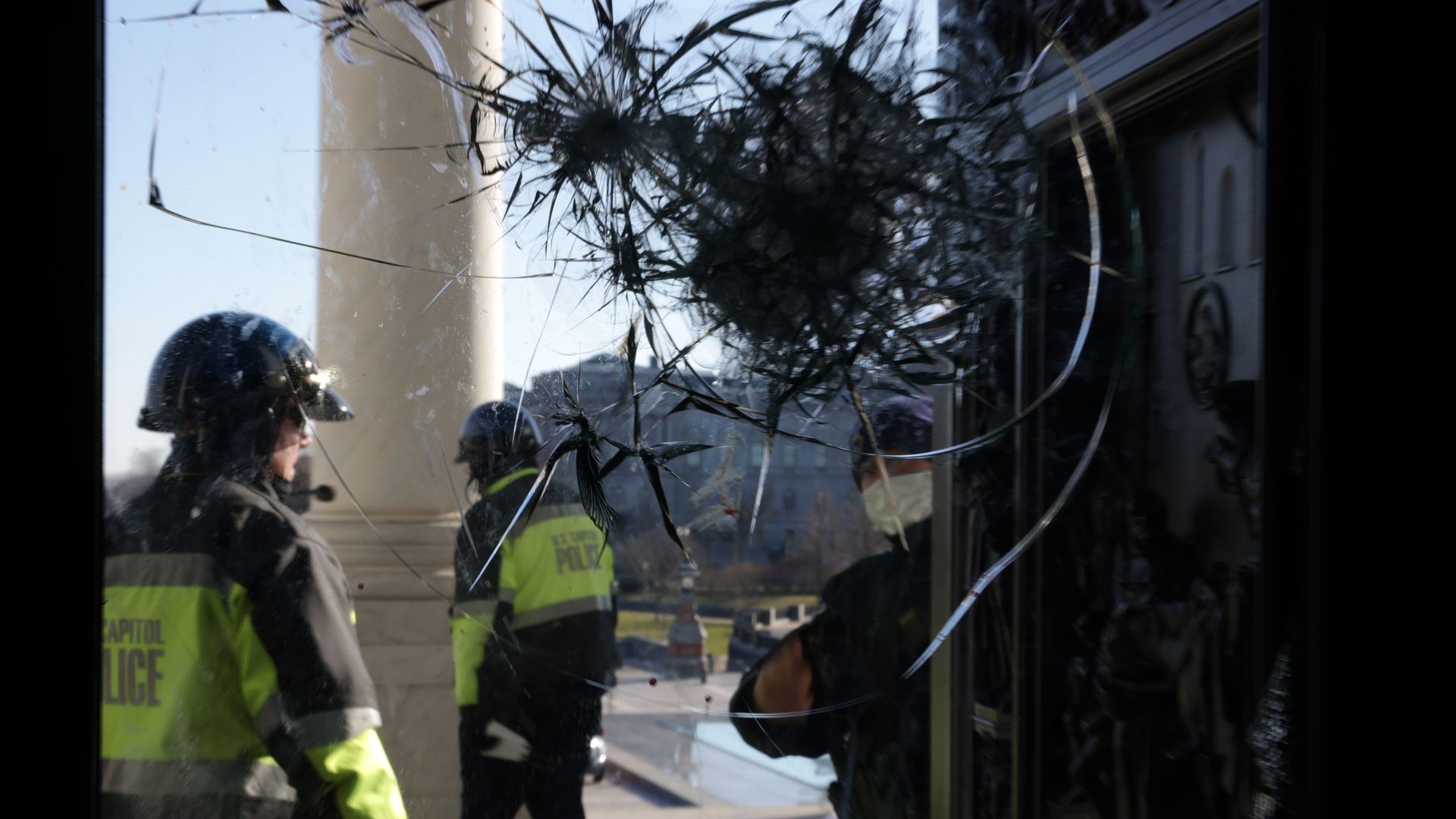 Officers stand behind a pane of broken glass with a column of the Capitol behind it