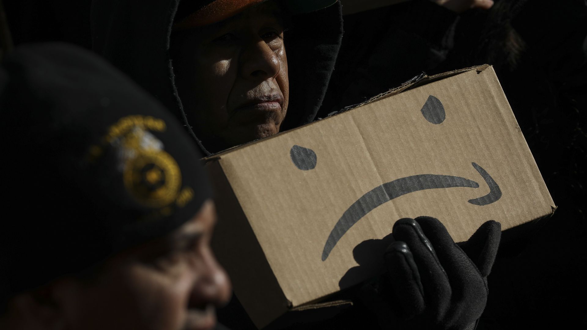 A man holds an upside-down Amazon logo with two eyes, made to look like a sad face