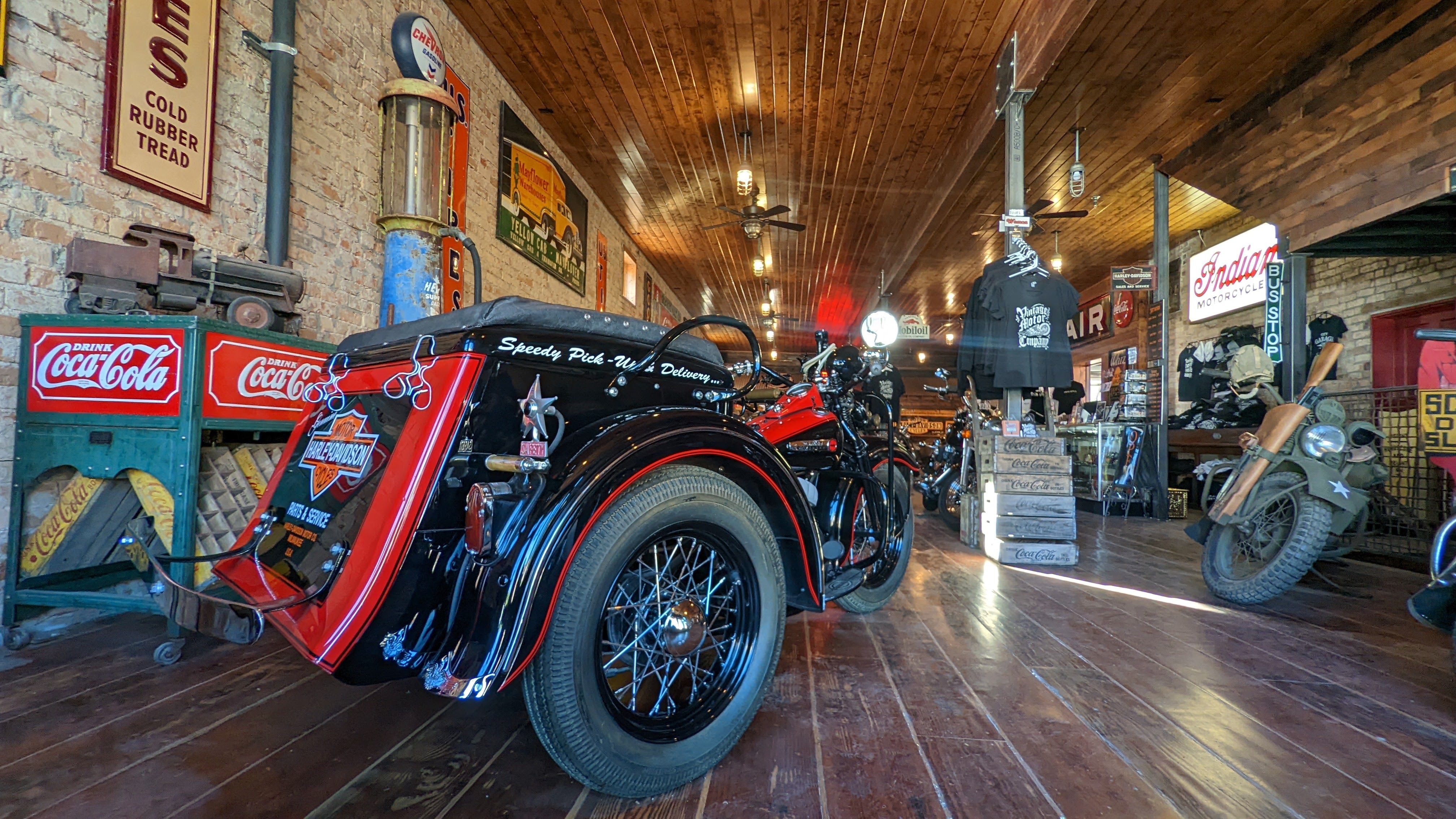 Antique motorcycles fill a room with a wood floor, wood ceiling and brick walls.
