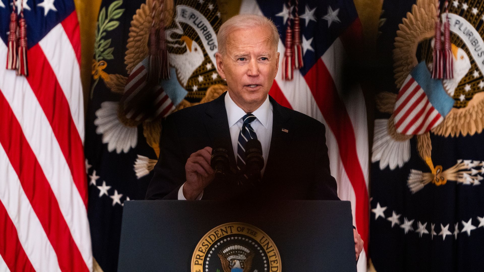 President Biden speaks at a podium with the presidential seal and flags in the background