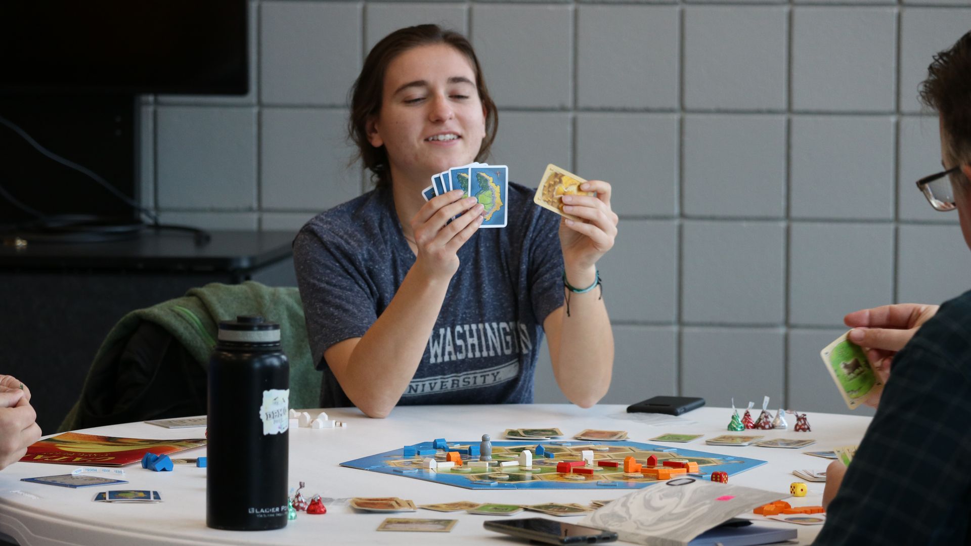 A woman holding cards playing Catan