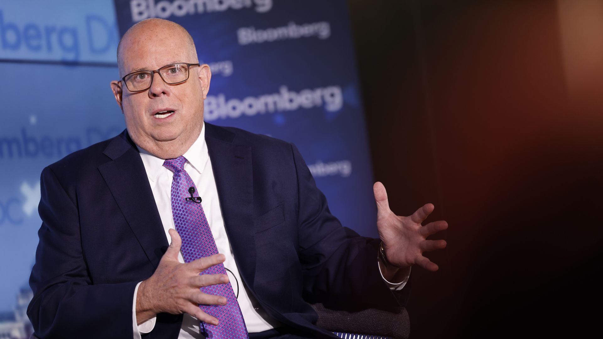 Larry Hogan, wearing a blue suit, white shirt and purple tie, in front of a blue Bloomberg backdrop.