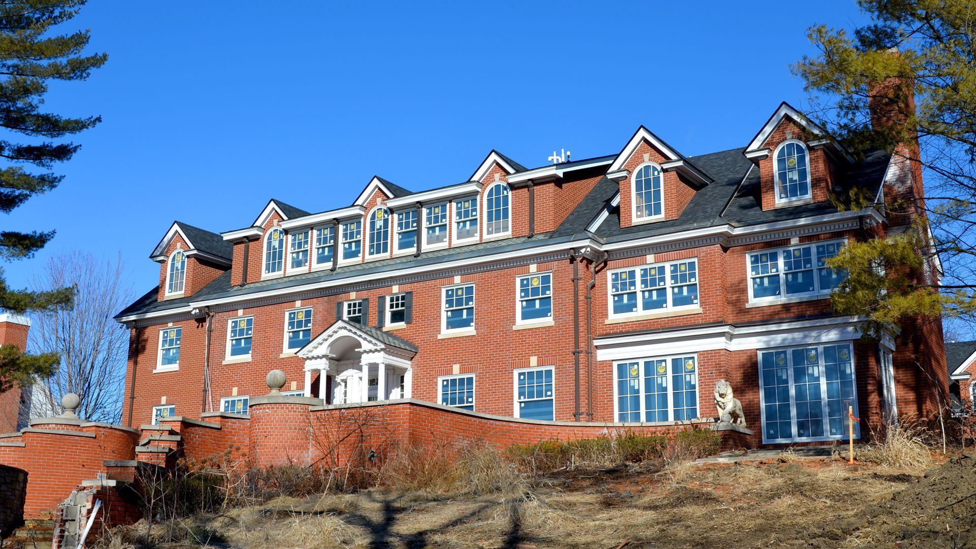 Brick house with four garret windows at the top and two floors visible behind a brick wall. 