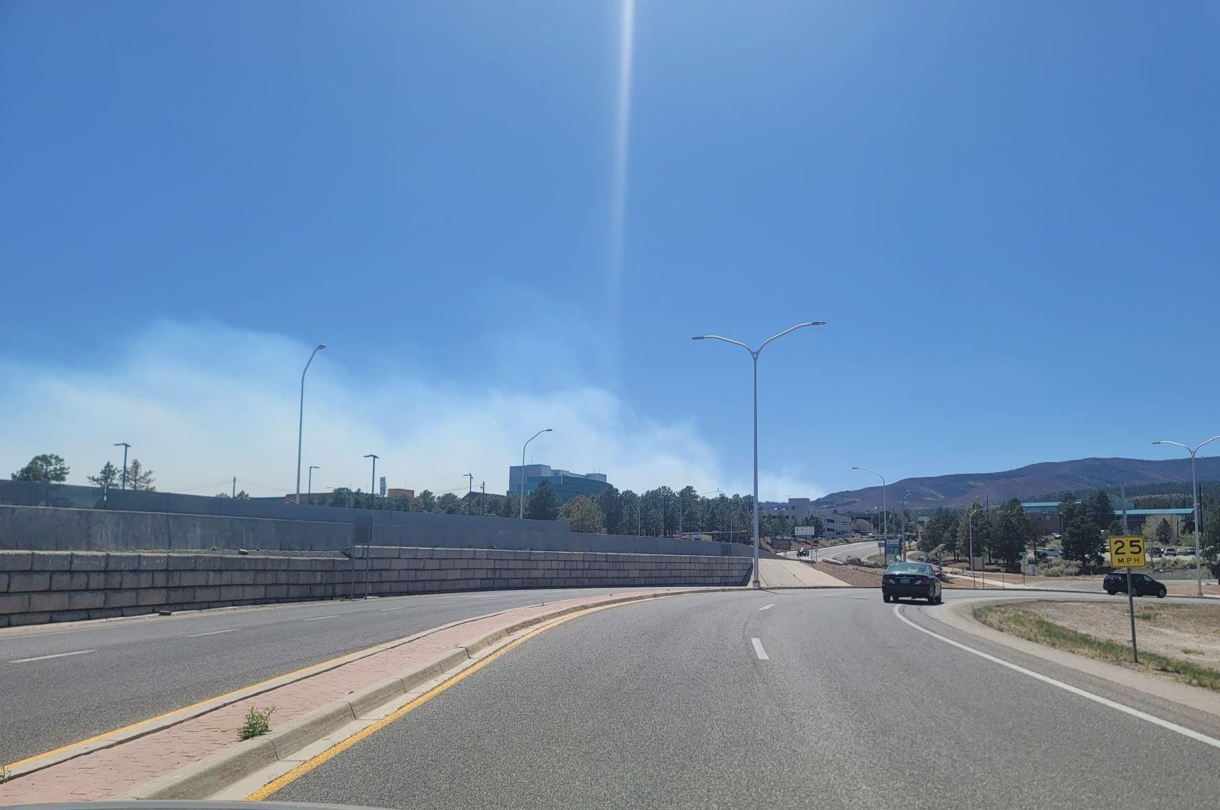 Smoke from the Cerro Pelado Fire as seen from Los Alamos as cars drive on a highway.