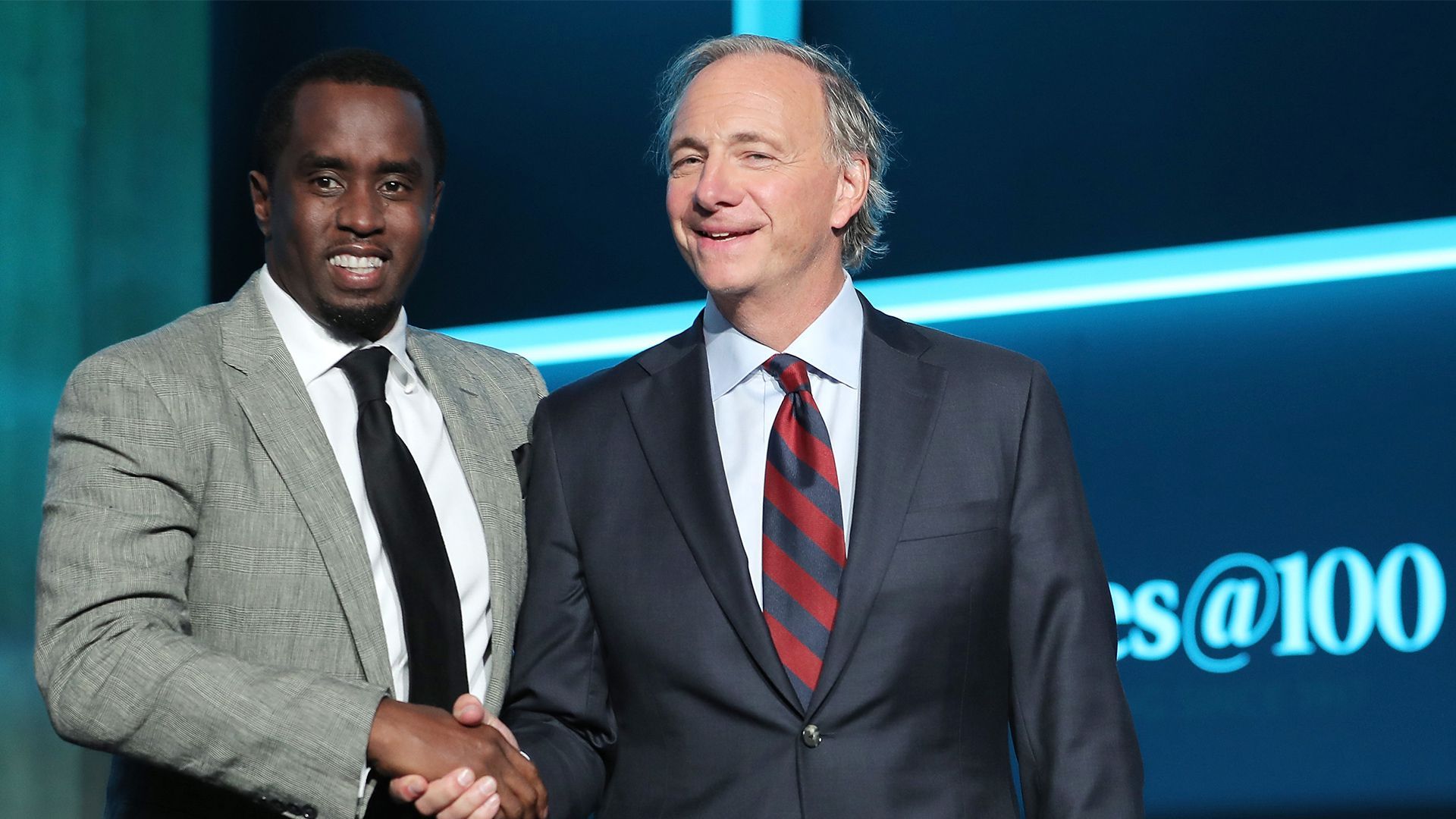 In this image, Dalio and Diddy stand together and shake hands while wearing suits