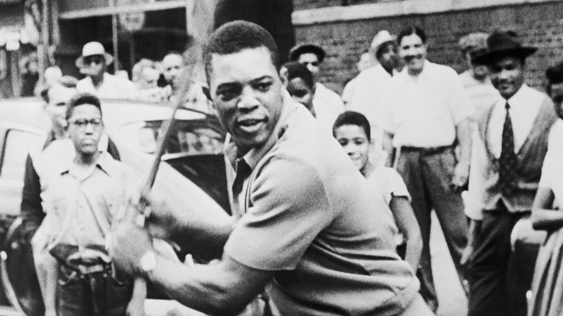 Photo of Willie Mays holding a bat in position as boys and men watch behind him