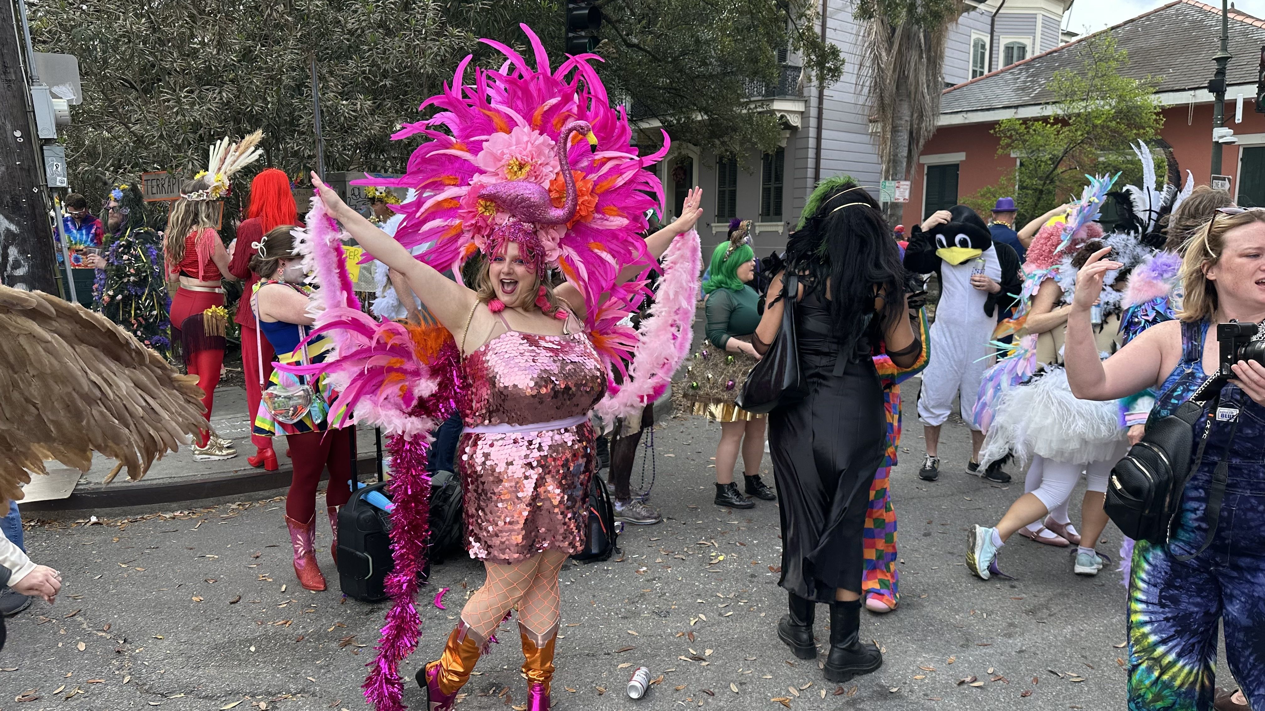 A woman dressed as a flamingo with a large pink feathered headdress smiles for the camera.