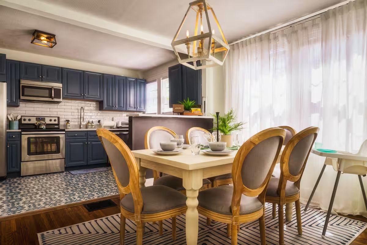 Kitchen table and chairs in a dining room with an open kitchen behind it with blue cabinets.
