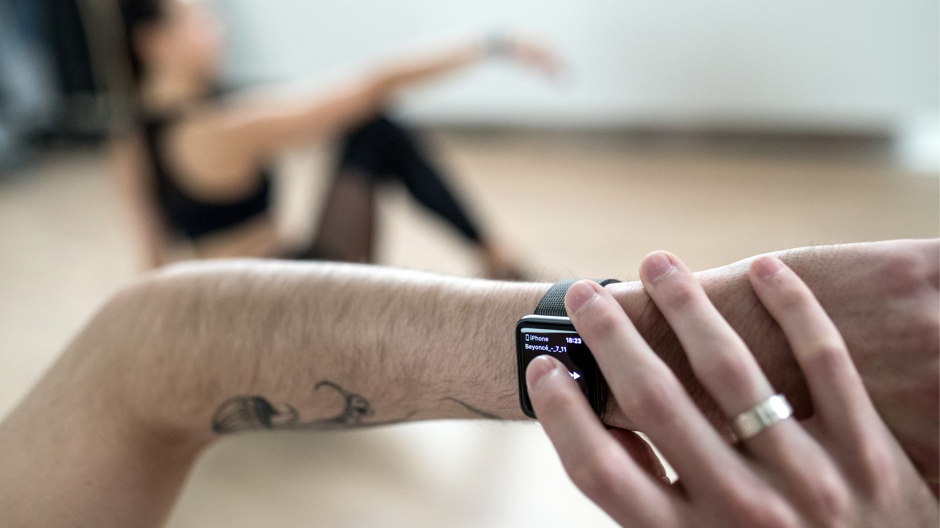 Someone's hand touching their apple watch with a blurred figure stretching or doing yoga in the background.