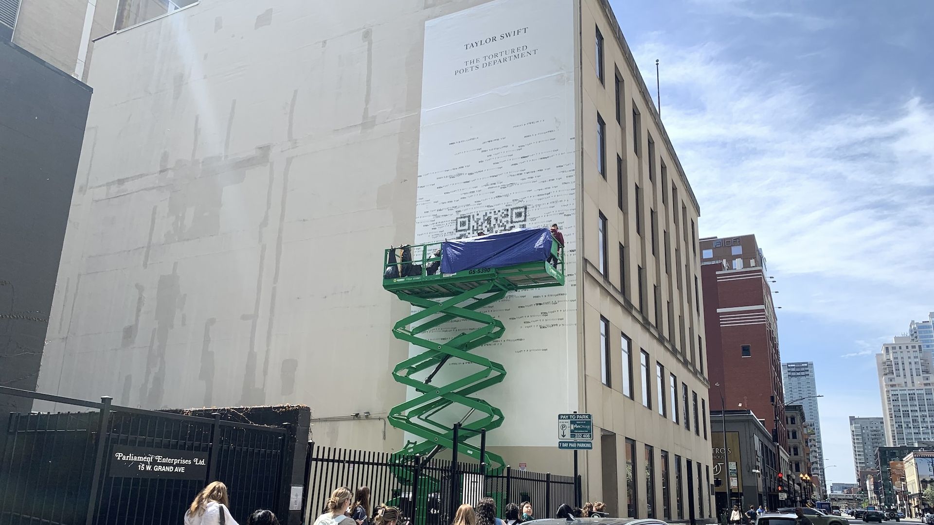 Billboard with QR code for Taylor Swift with people lined up on the sidewalk underneath.