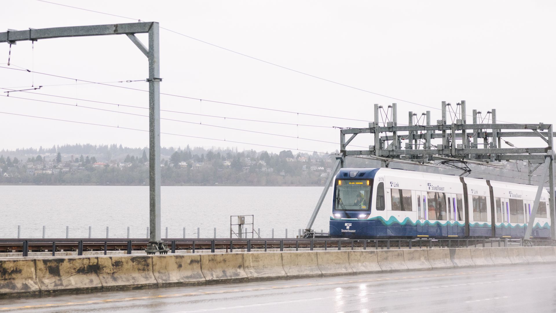 A Sound Transit train crosses tracks over the I-90 bridge with Lake Washington in the background and some fog shrouding the bridge.
