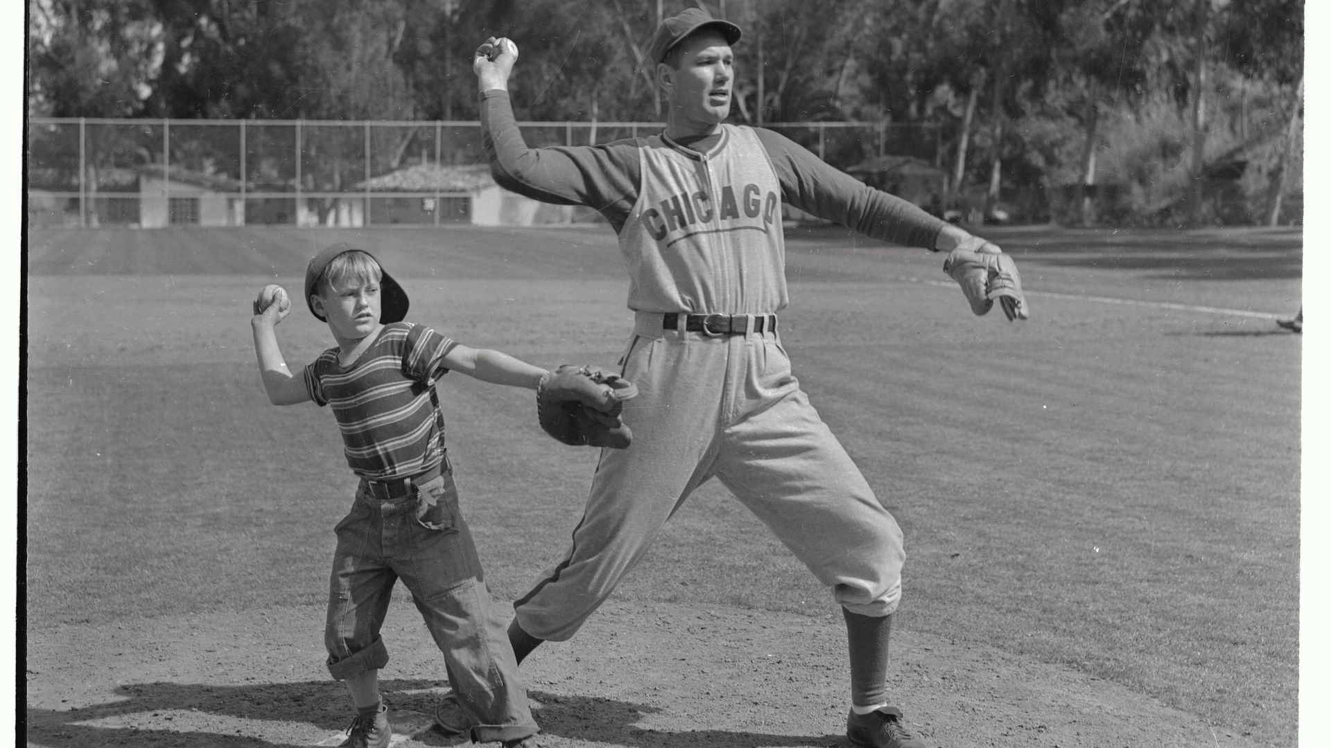 Photo of a baseball player teaching a kid how to throw a baseball. 