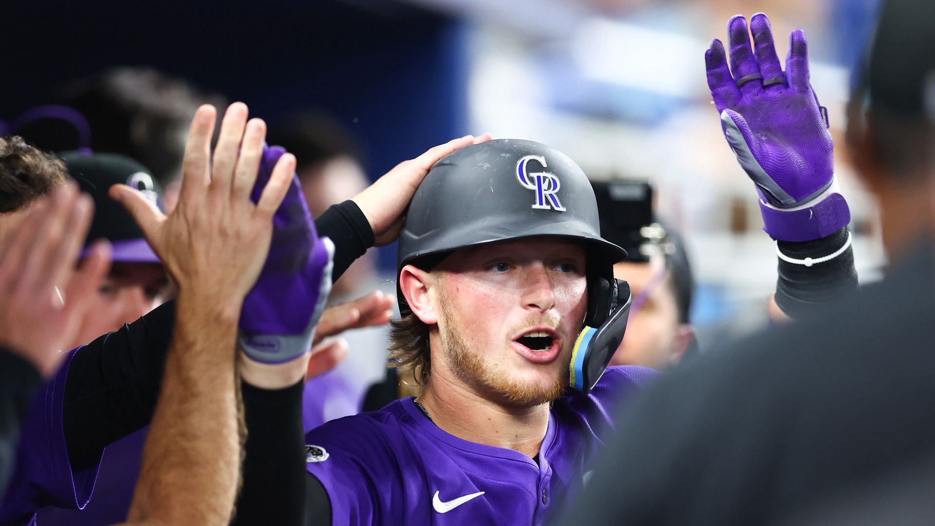 A man high-fives other people in a crowd while wearing a black helmet and purple uniform. 