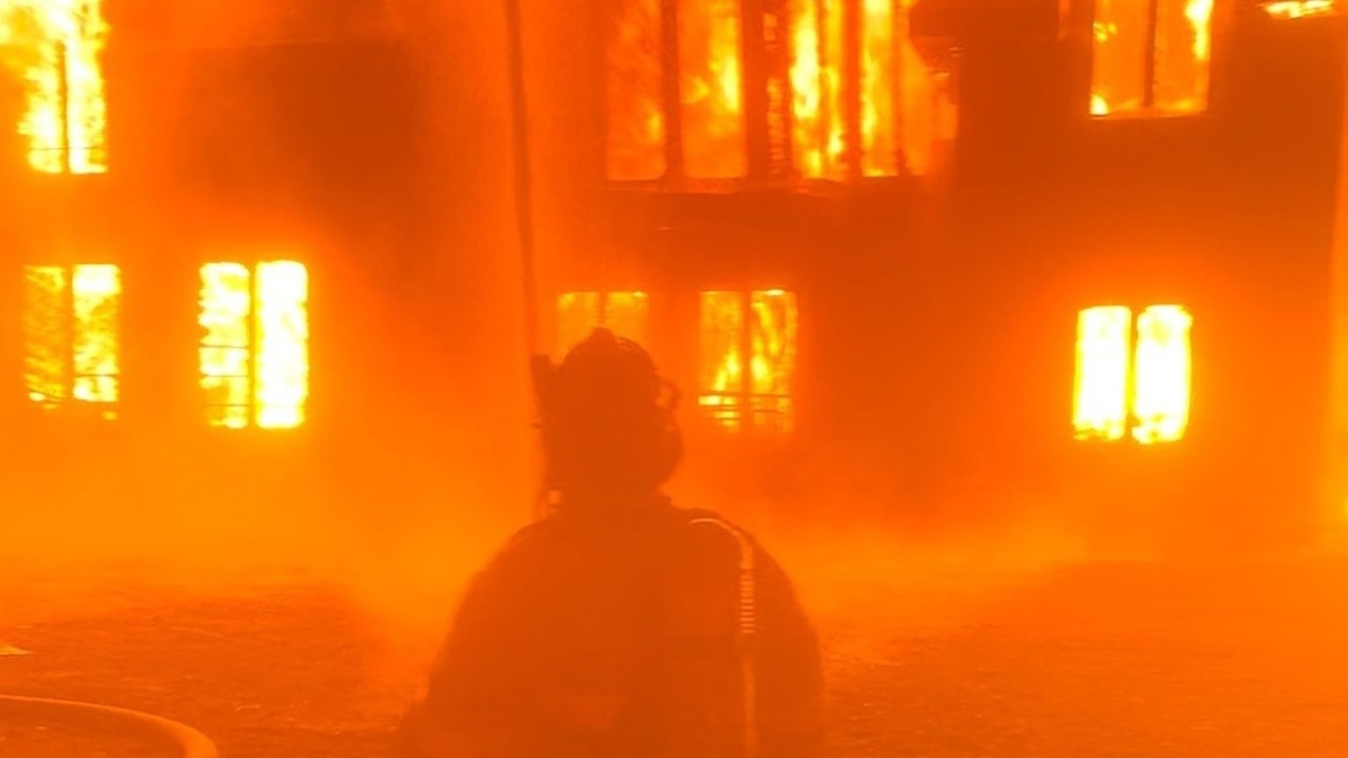 A fire fighter in front of a burning house.